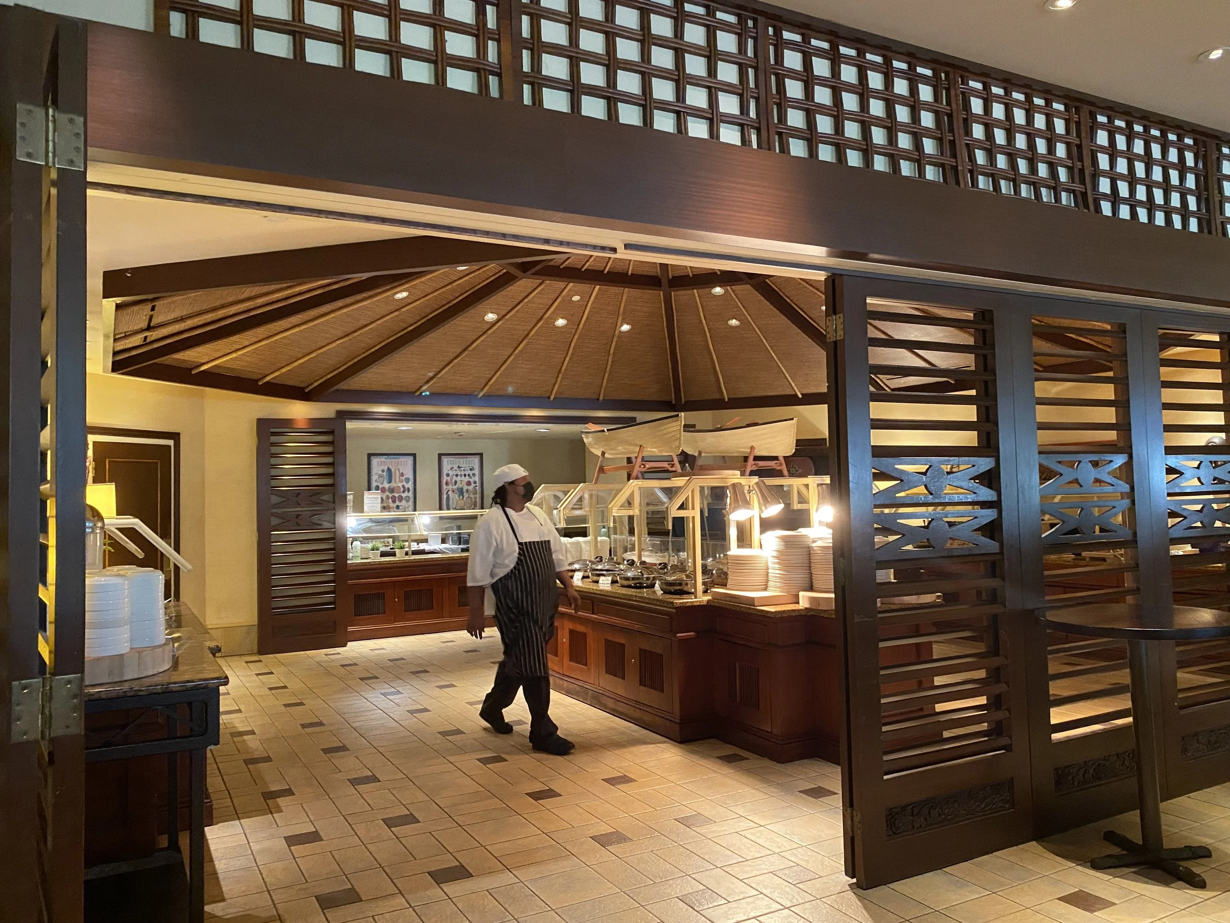 Chef standing near a buffet station in a restaurant with wooden decor and a tiled floor.