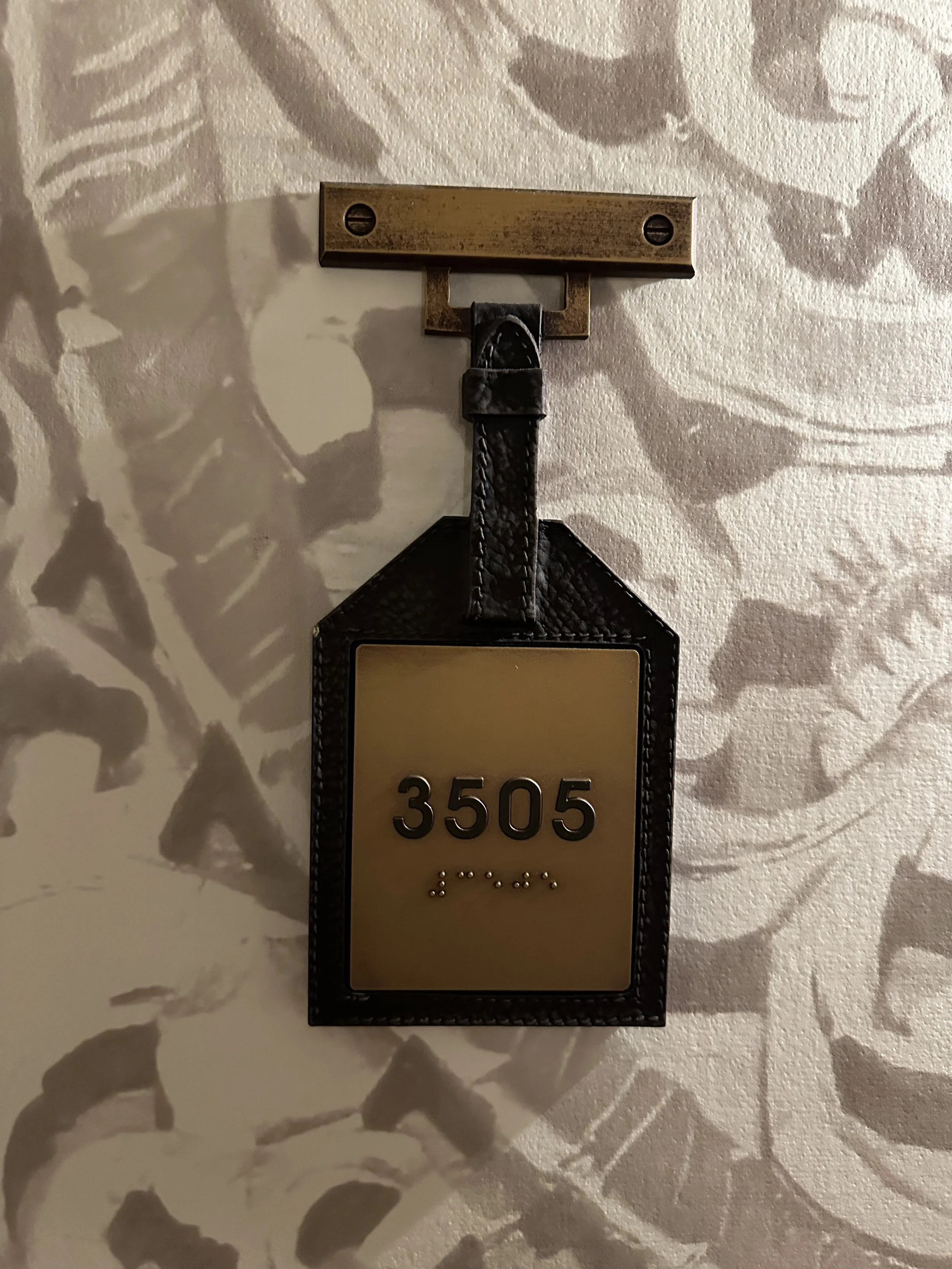 Hotel room keychain with room number 3505 hanging on a wall hook with decorative wallpaper in the background.