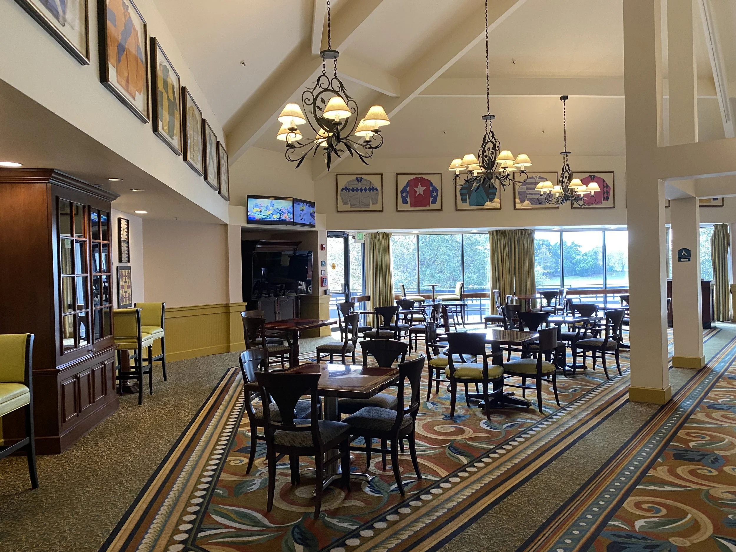Interior of a cheerful restaurant or cafe with large windows, colorful artwork, chandeliers, and a patterned carpet.