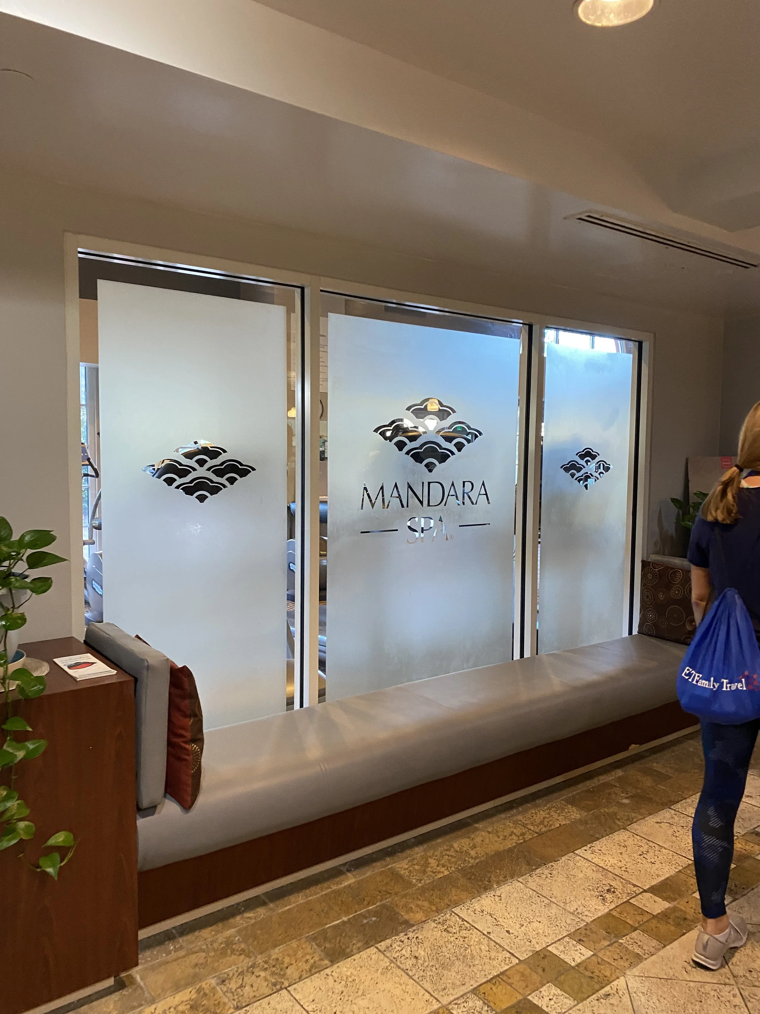 Lobby entrance with frosted glass window with logo and text for Mandara Spa, and a woman standing nearby with a blue bag.