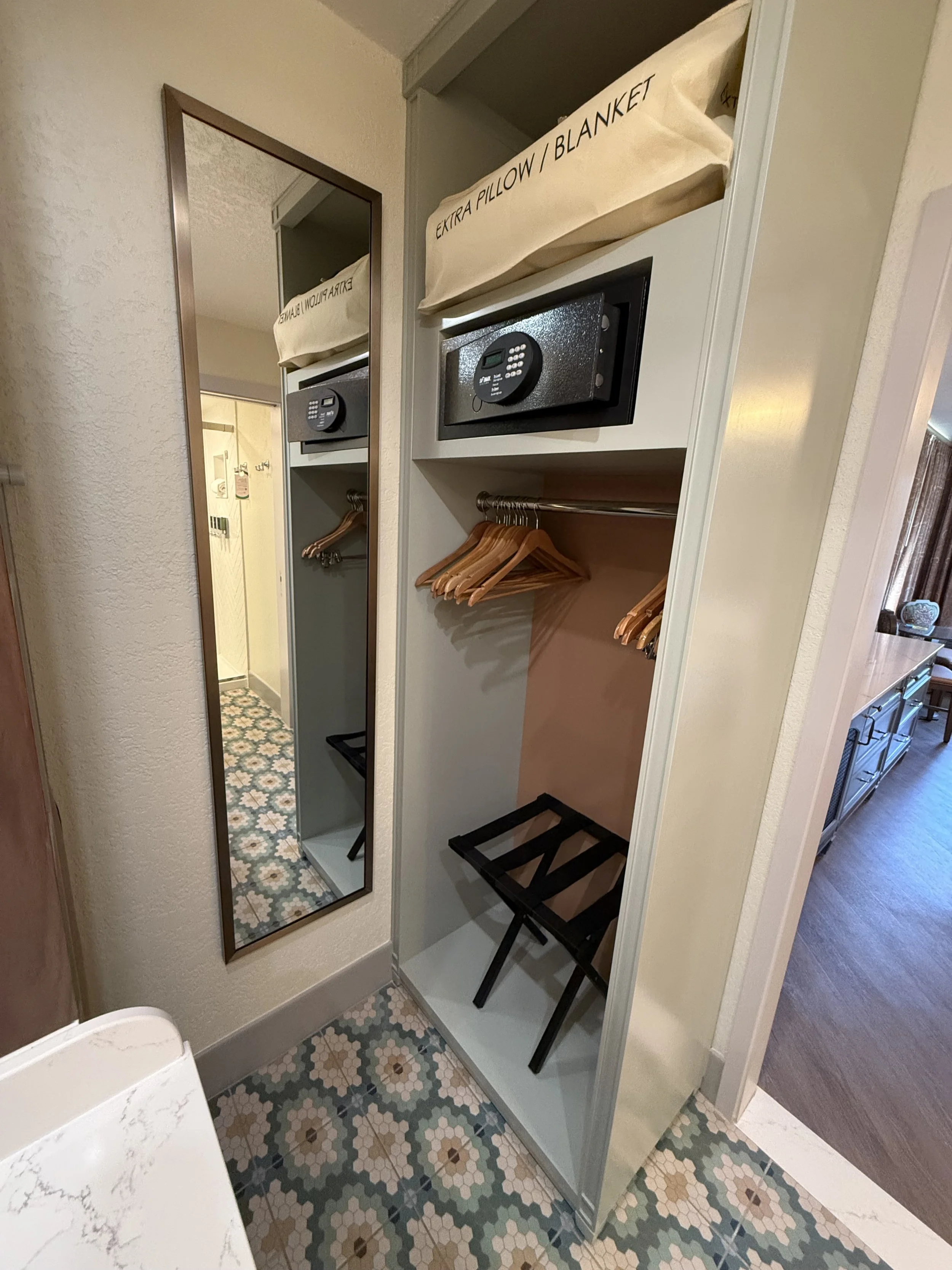 Hotel closet with a safe, an extra pillow/blanket in a bag labeled 'extra pillow/blanket,' a mirror, and a luggage rack.