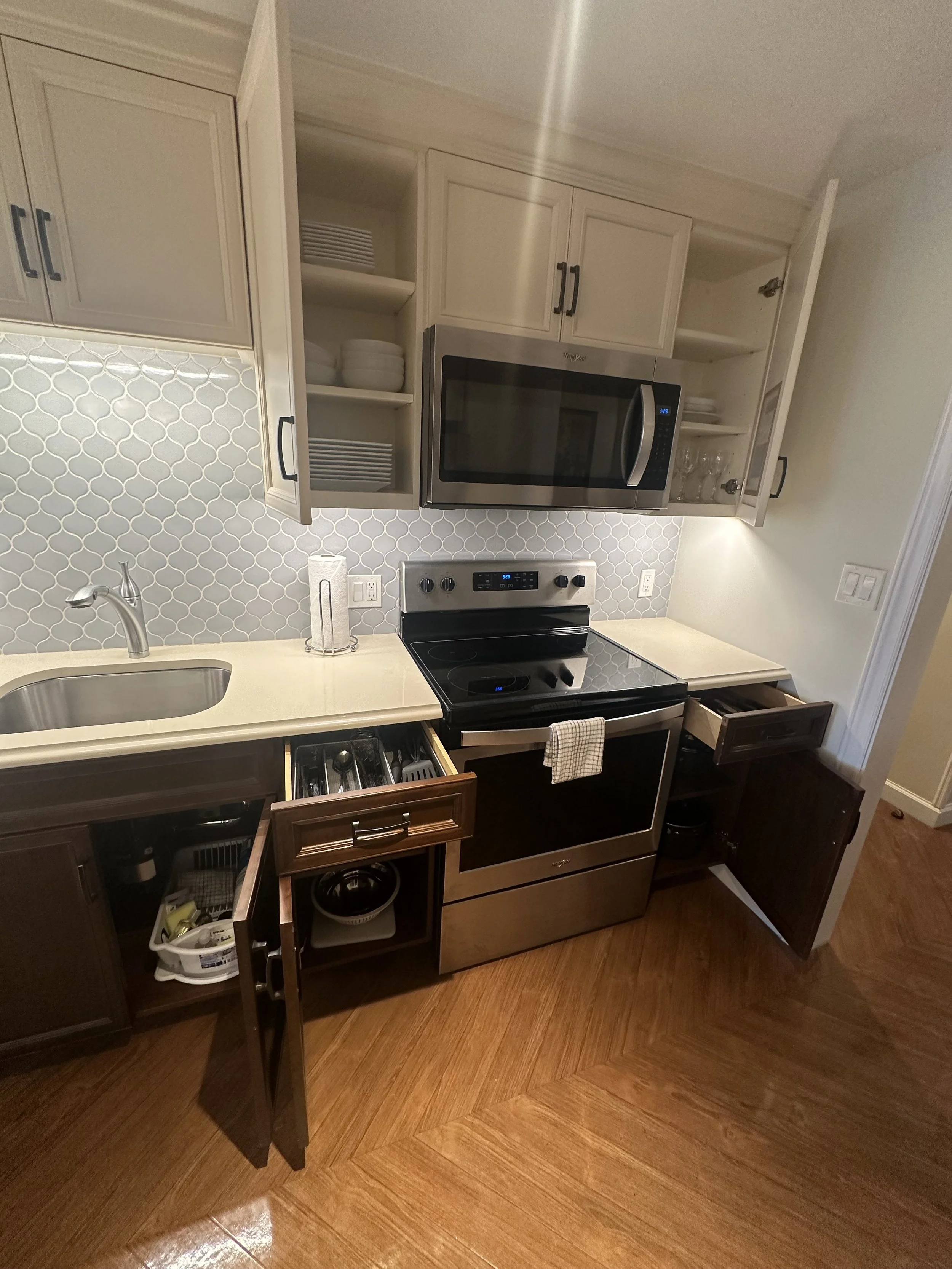 Kitchen with open cabinet doors, stainless steel microwave, stove, and wood flooring.
