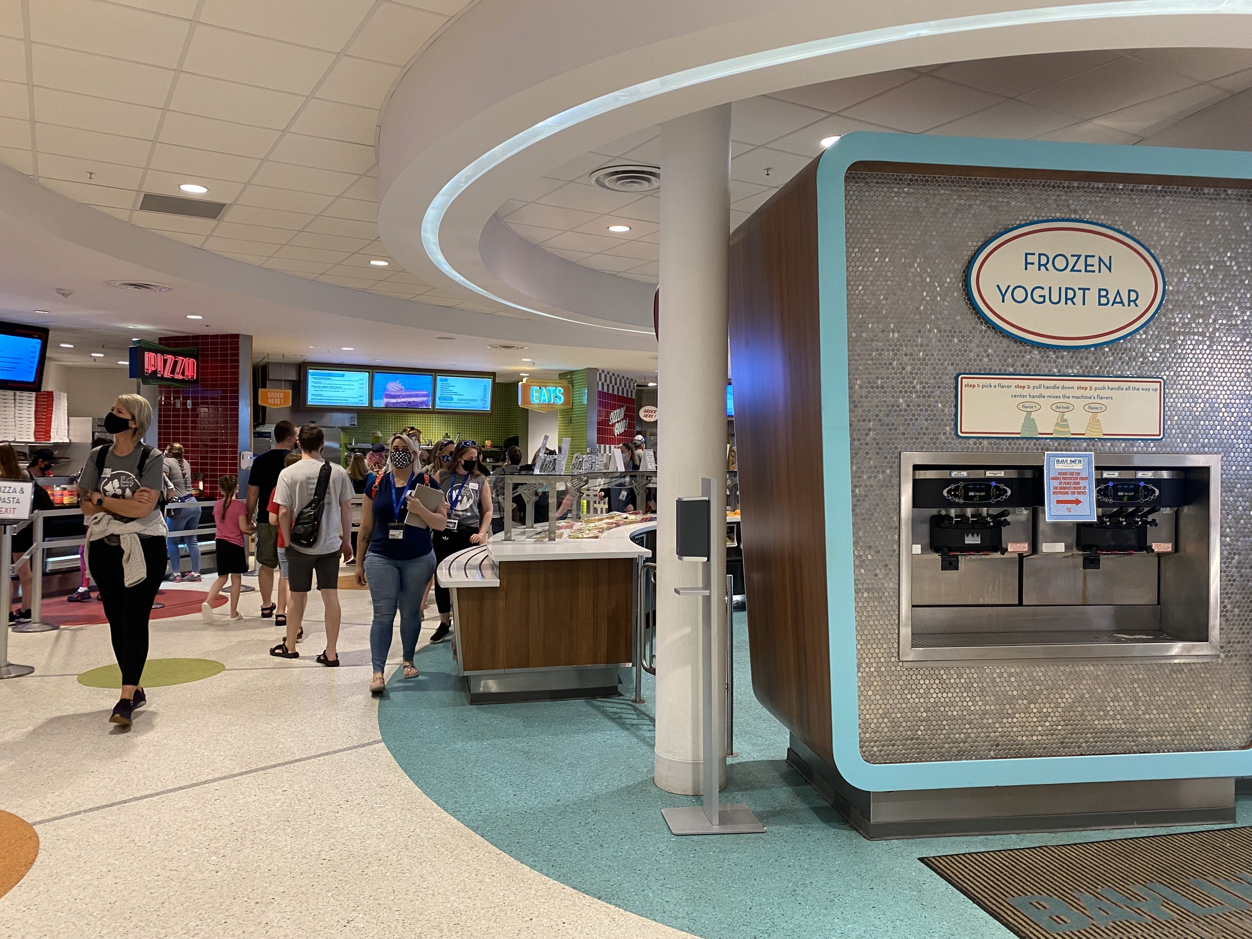 Frozen yogurt bar in a busy food court with people wearing masks.