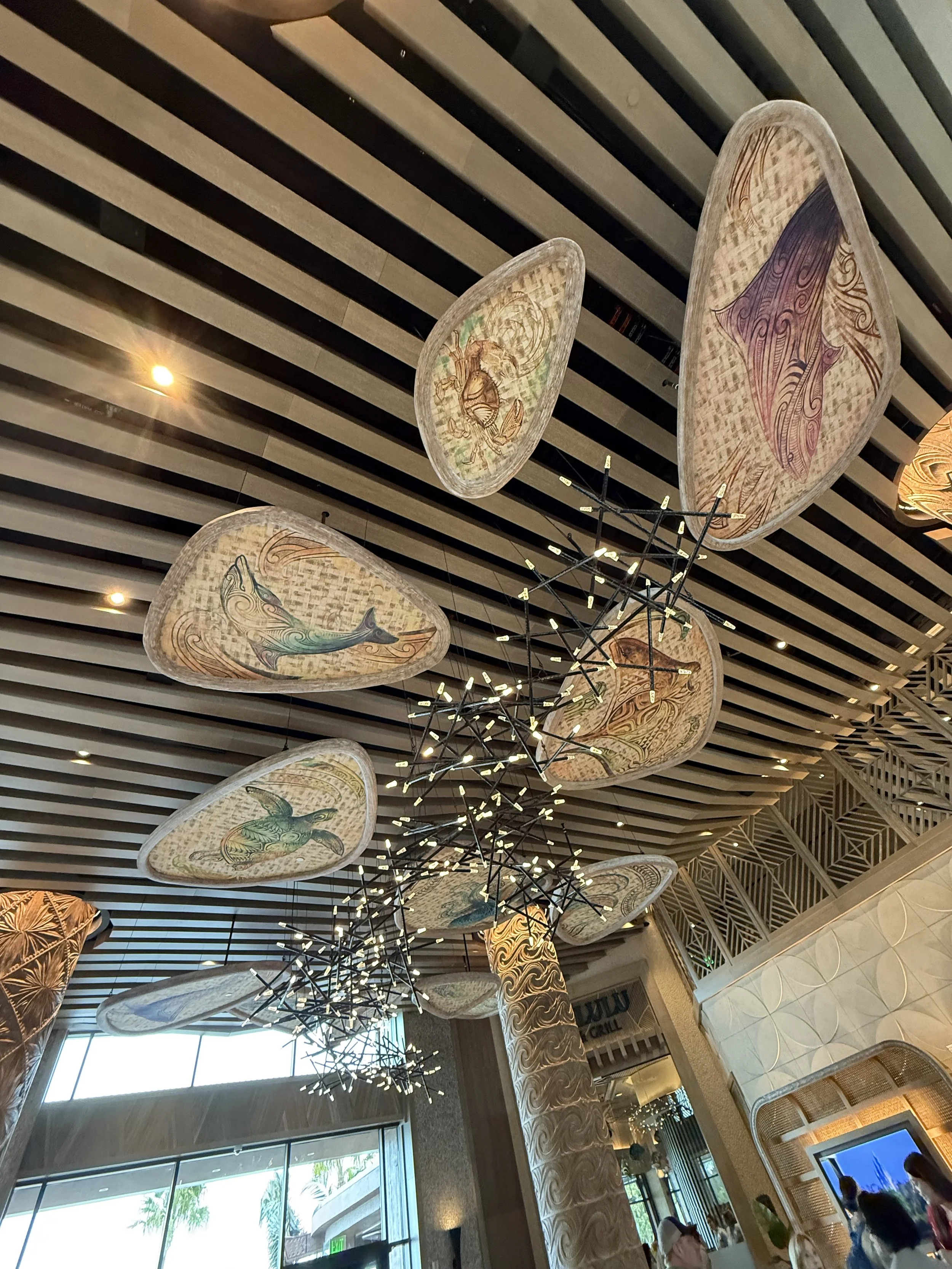 Decorative capiz shell ceiling with aquatic-themed artwork, modern chandelier, and natural light inside a building.