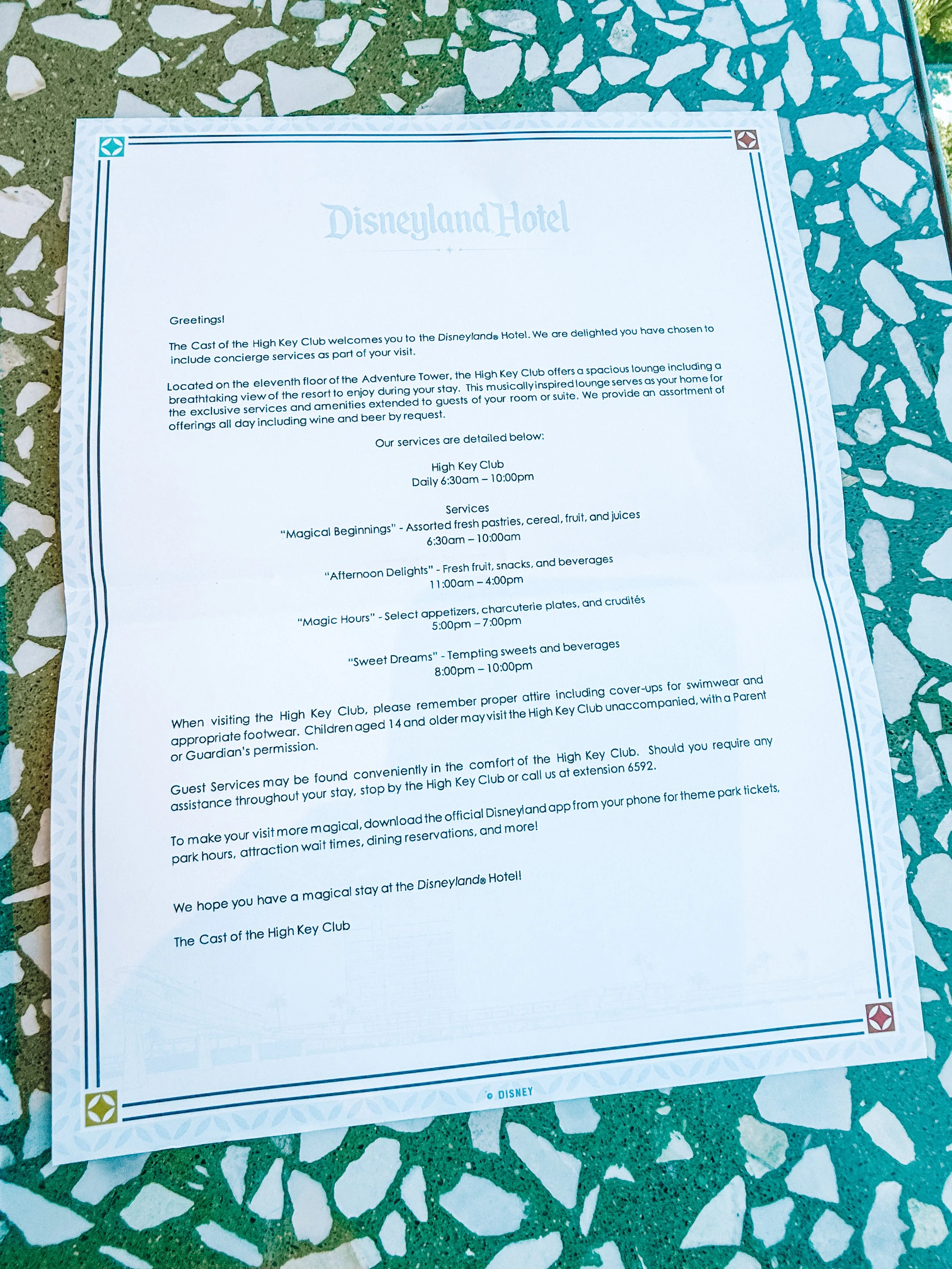 A printed informational sheet about services and guidelines at the Disneyland Hotel, placed on a colorful mosaic table.