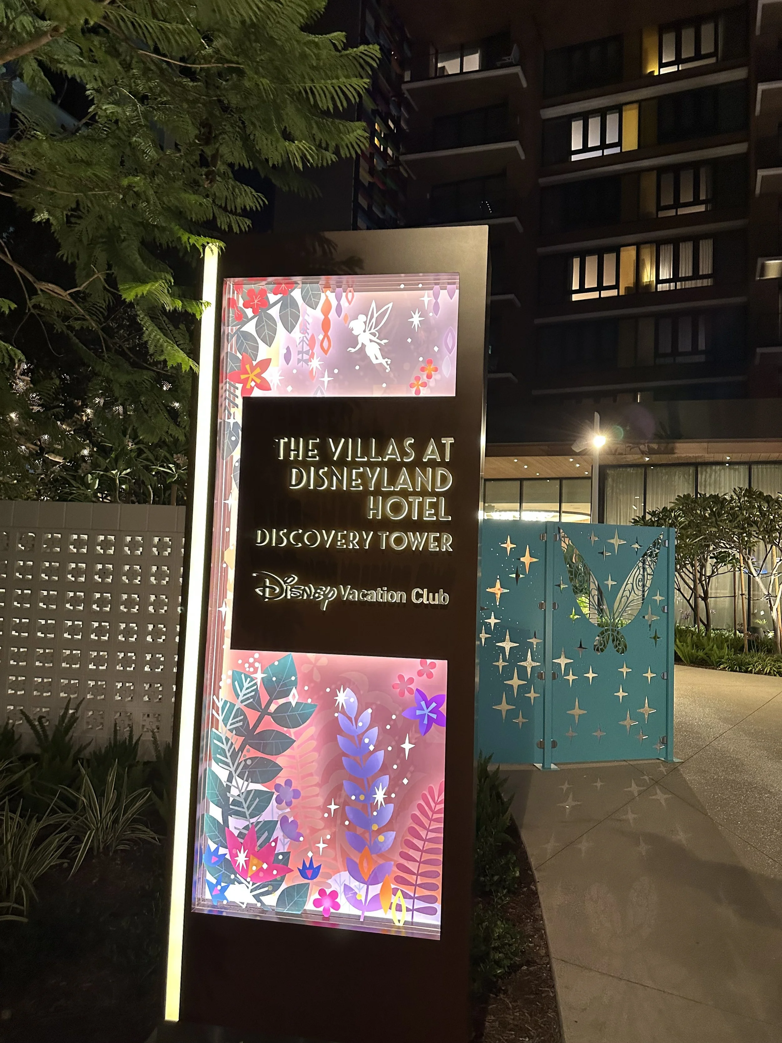 Illuminated sign for The Villas at Disneyland Hotel and Discovery Tower, featuring colorful floral and fairy illustrations at night.