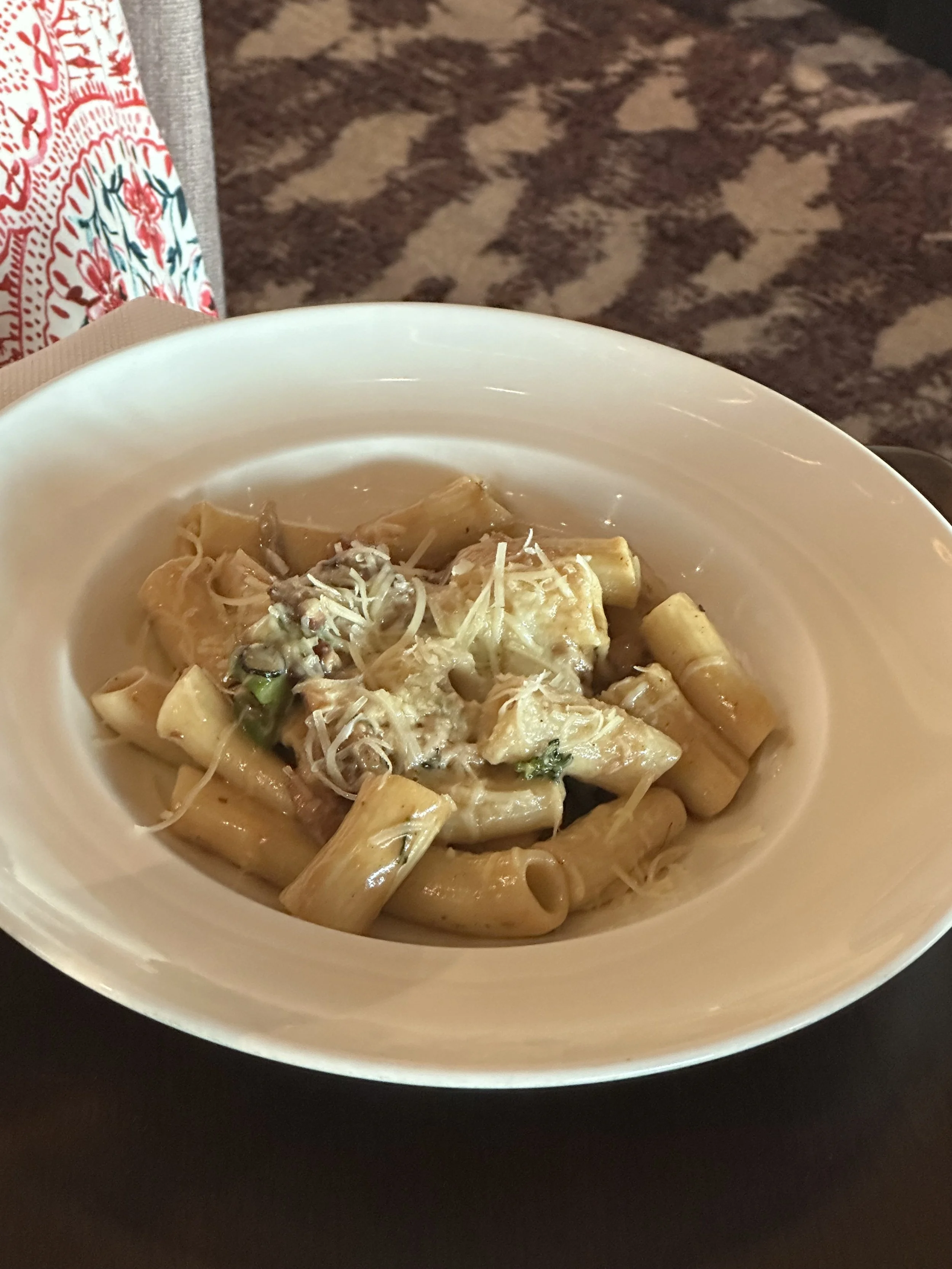 Creamy pasta with chicken and shredded cheese in a white bowl.