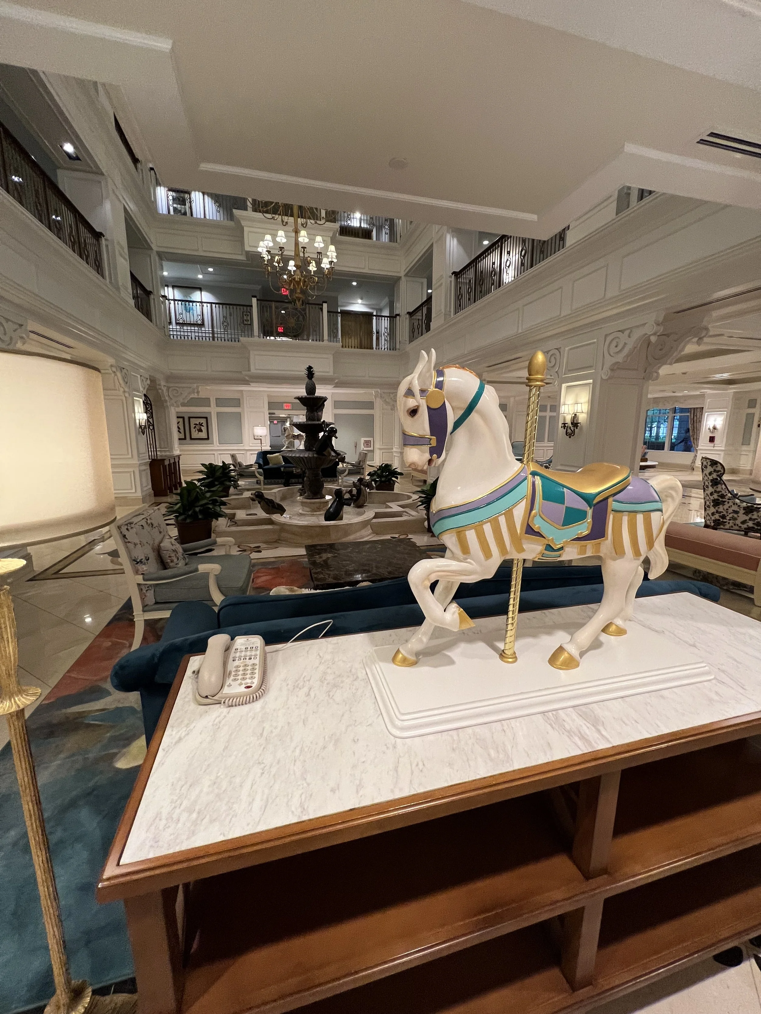 A decorative porcelain carousel horse on a marble-top table in a luxurious hotel lobby.