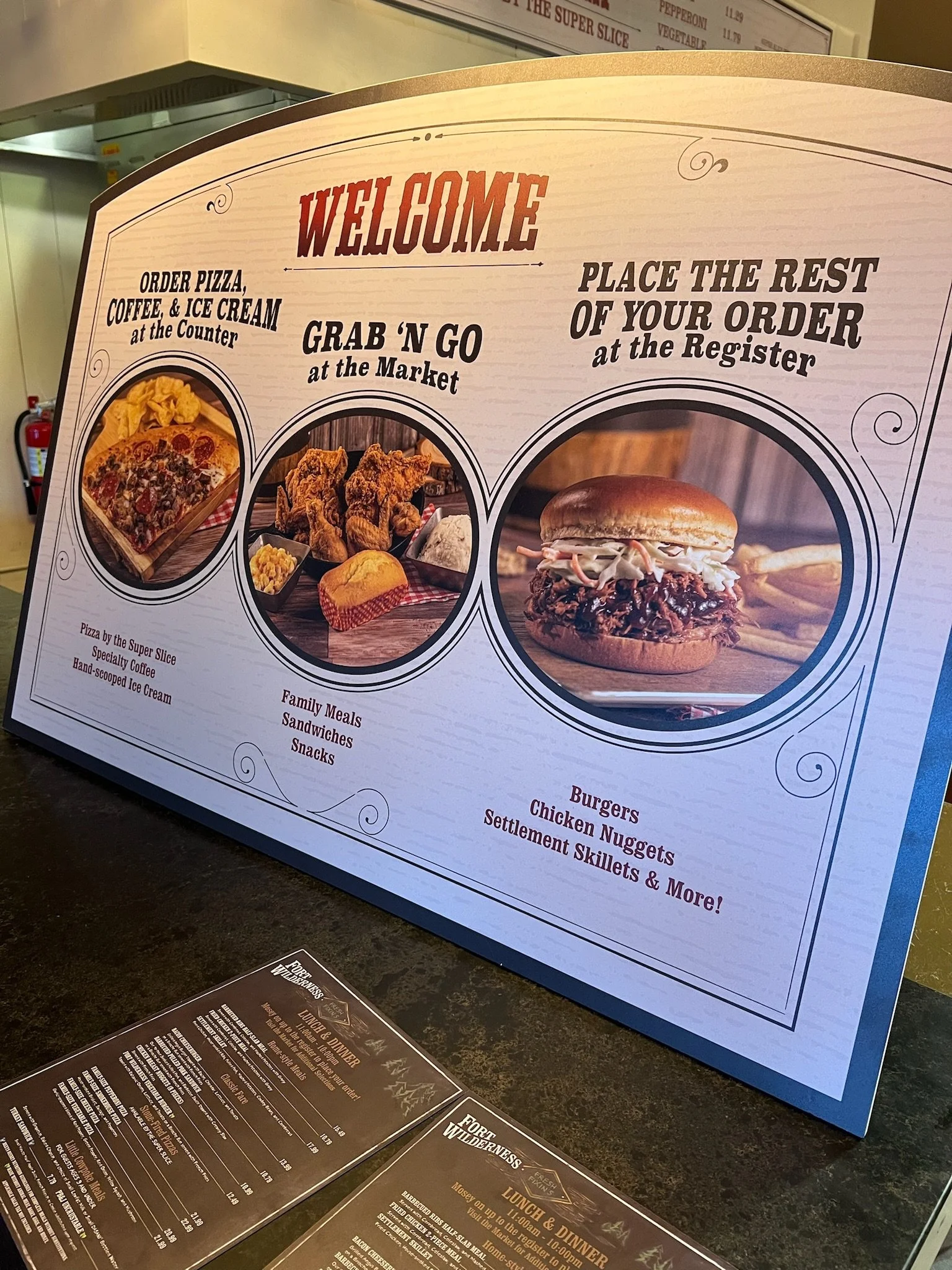A restaurant menu sign welcoming customers, with sections for ordering pizza, coffee, and ice cream at the counter, grab 'n go options at the market, and placing the rest of the order at the register. The sign features images of a pizza slice, fried 