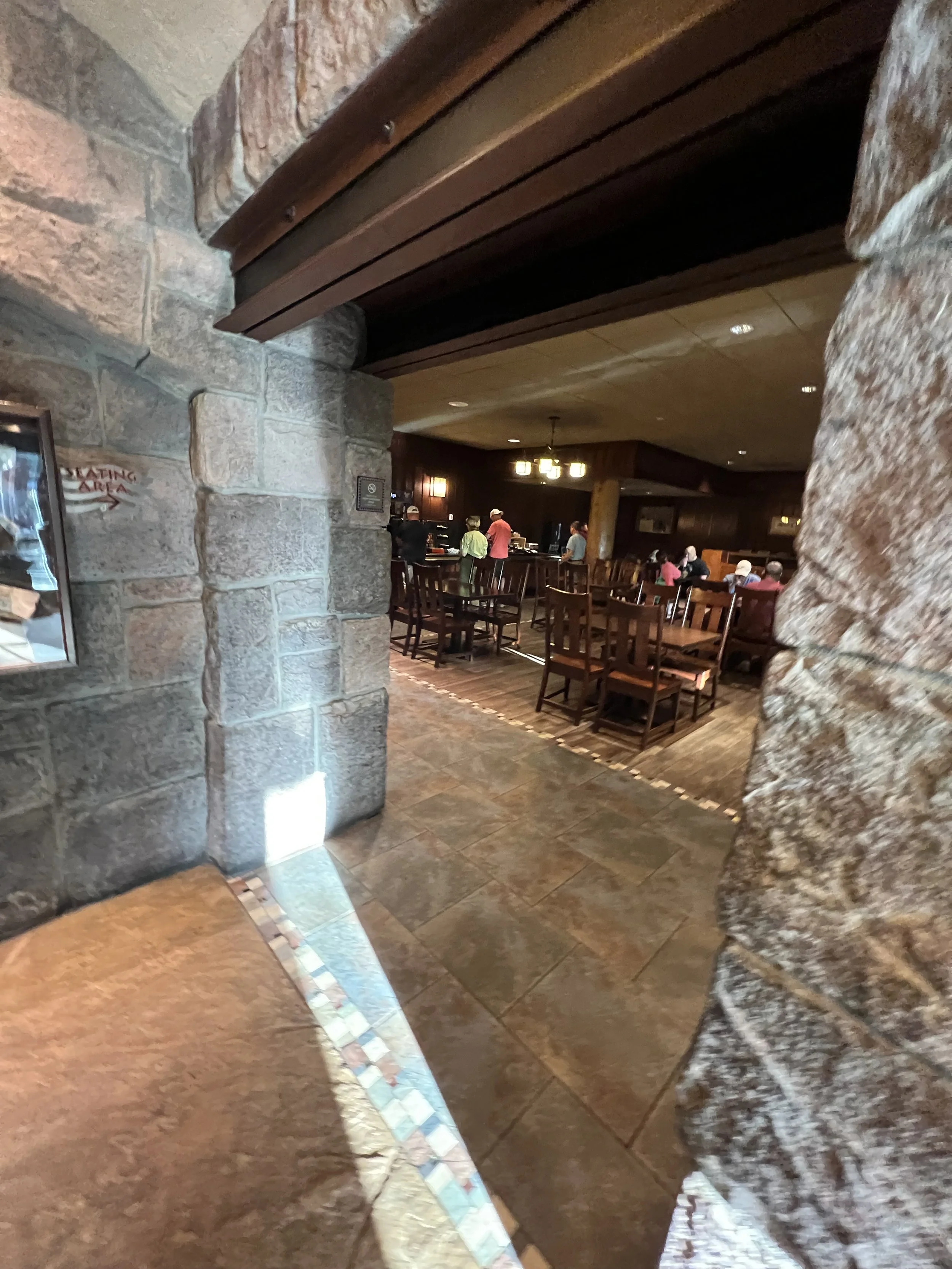 View of a restaurant interior with wooden tables and chairs, stone and wood walls, and a few customers dining.