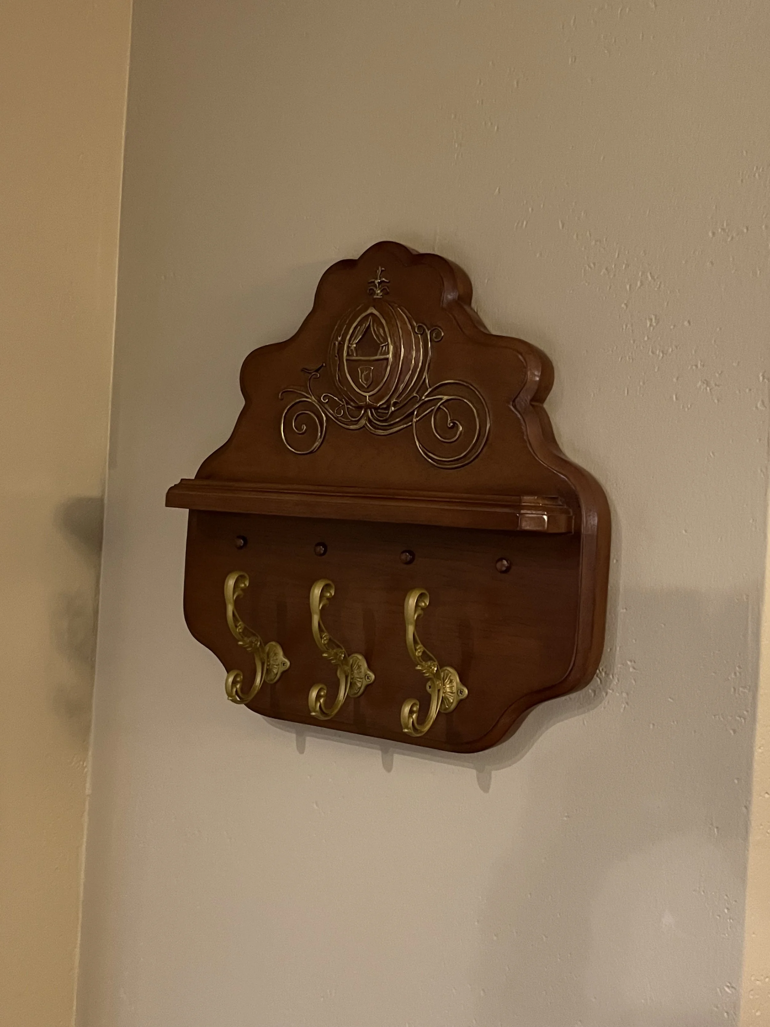 A wooden wall-mounted coat rack with three gold hooks and decorative metalwork at the top.