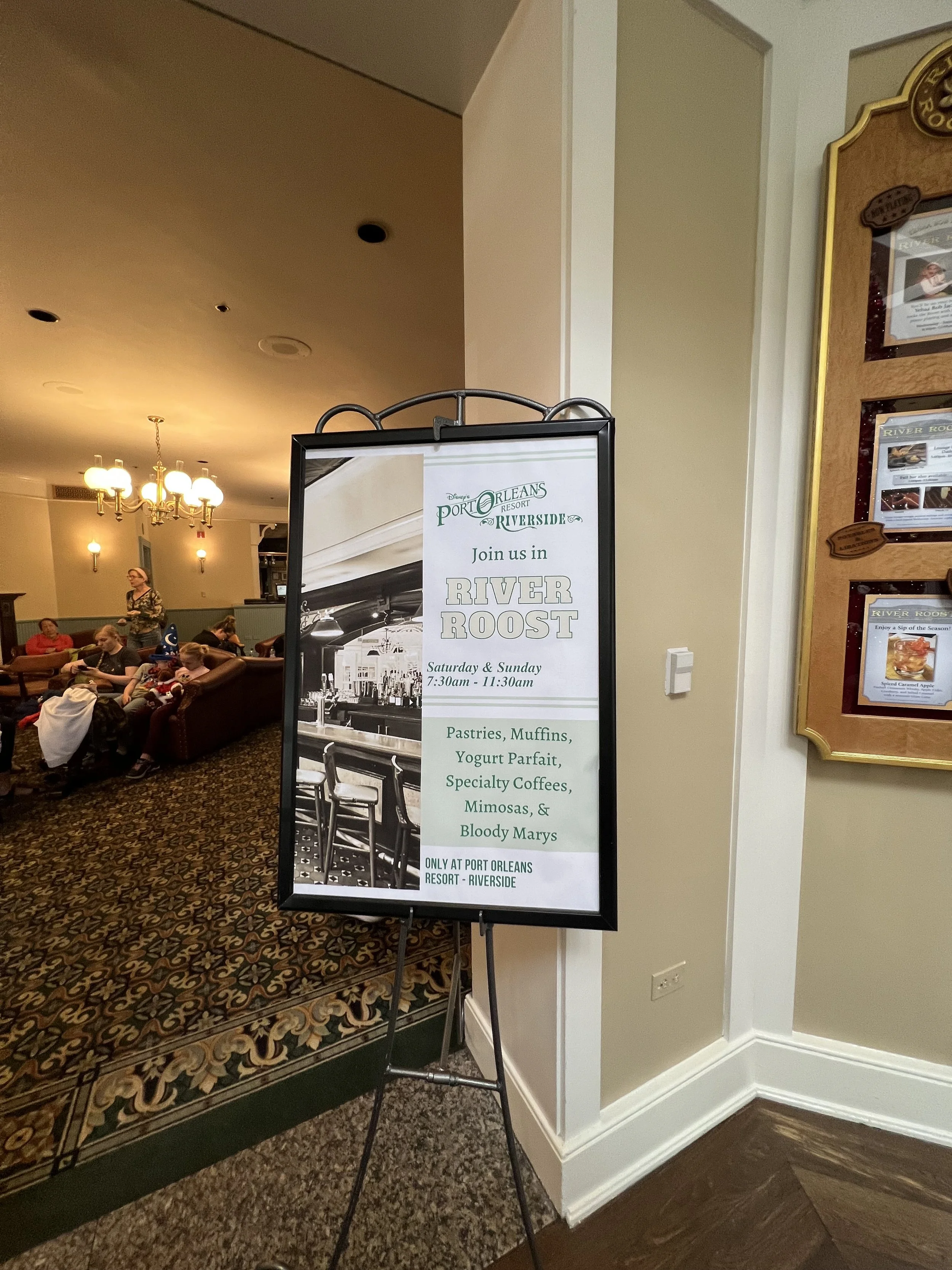 Sign promoting a breakfast event called River Roost at Port Orleans Riverside Resort, featuring pastries, muffins, yogurt parfait, specialty coffees, mimosas, and Bloody Marys, held on Saturday and Sunday from 7:30am to 11:30am.