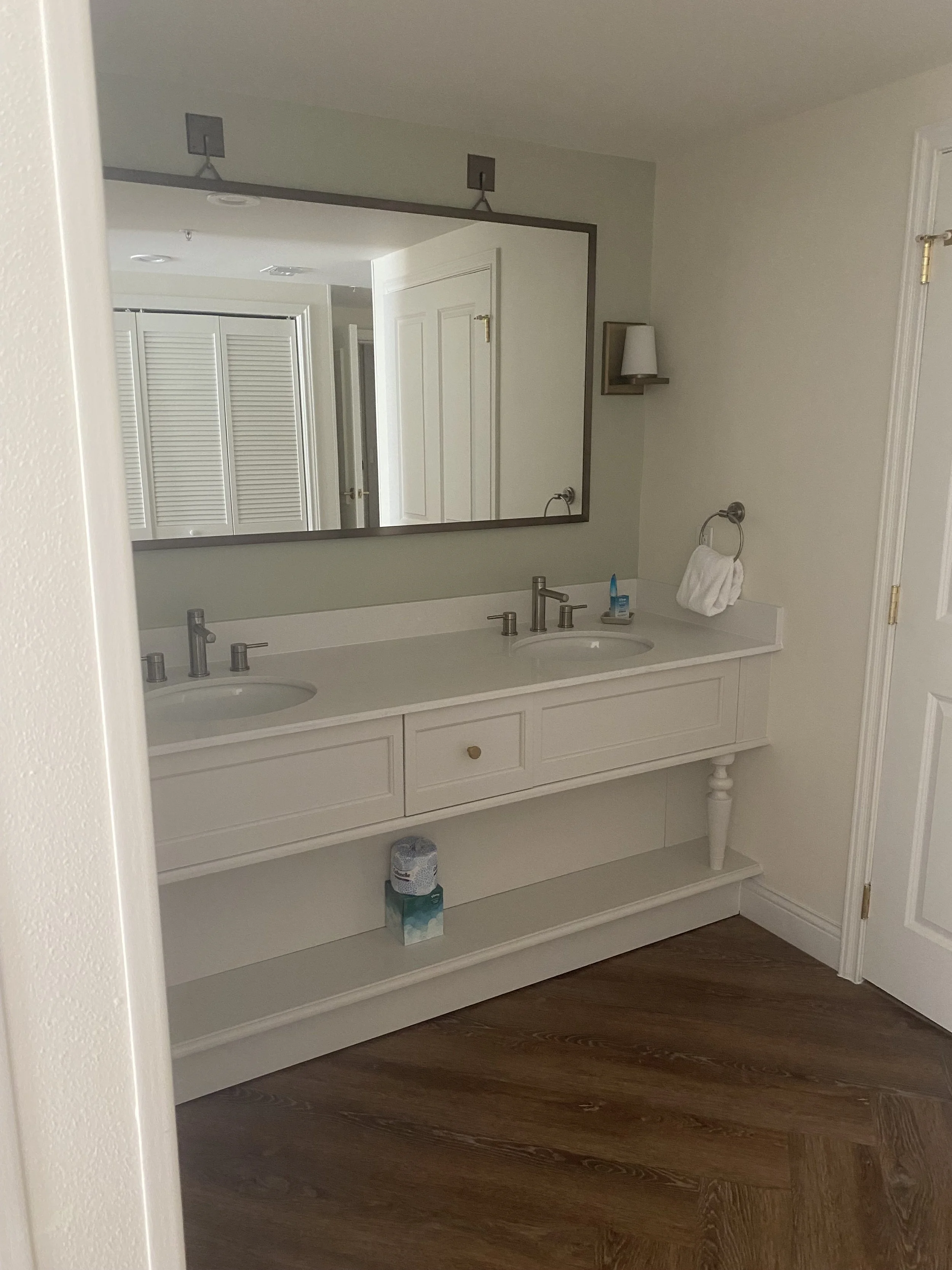 Bathroom with double sink vanity, large mirror, and wooden flooring.