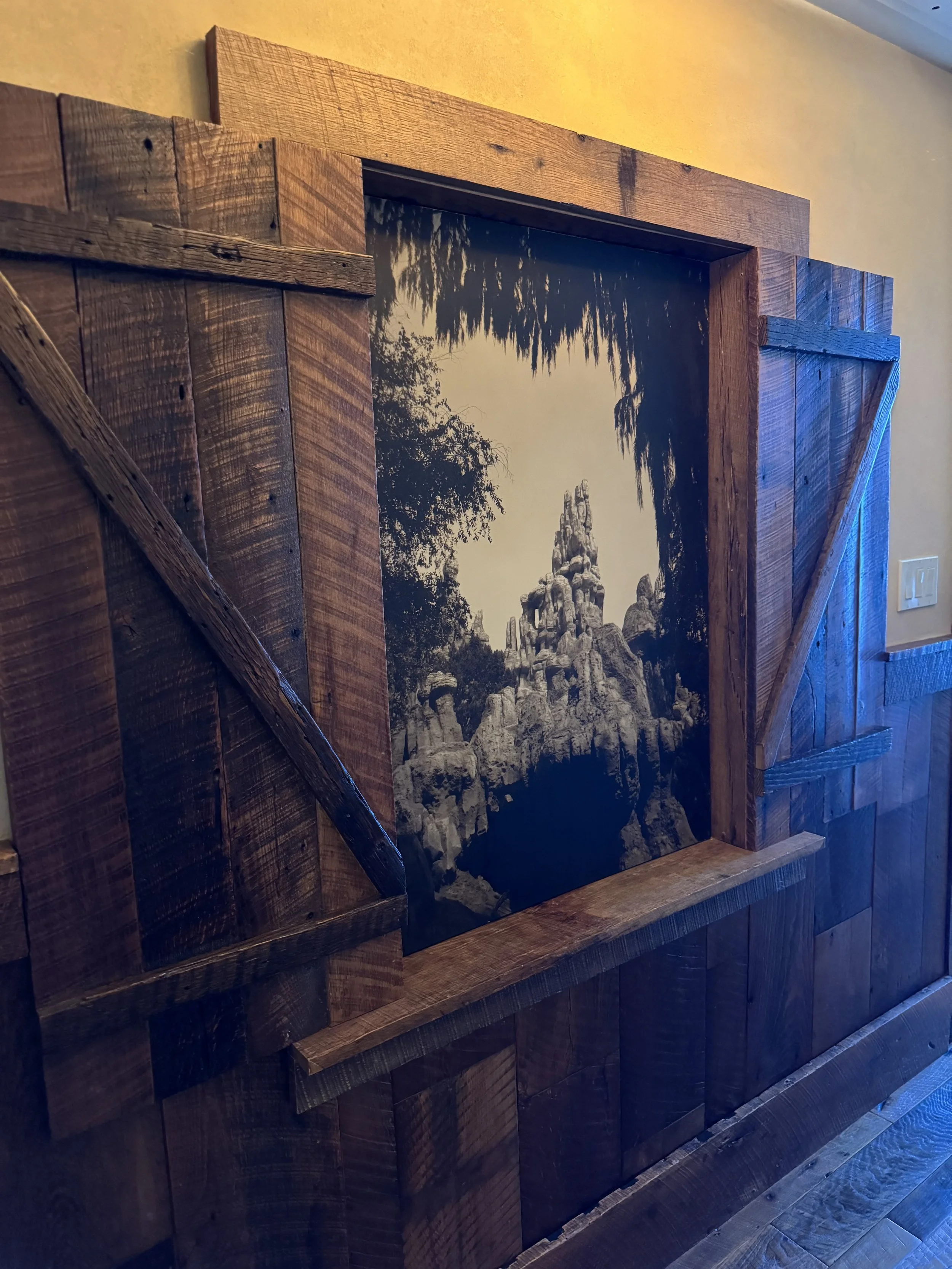 A framed black and white photo of rocky mountain peaks surrounded by trees, set in a wooden wall with barn-style sliding door hardware.