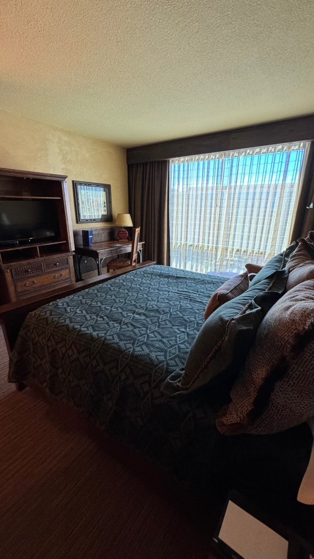 A hotel room with a bed, a chair, a desk, a lamp, a TV, and a window with curtains.