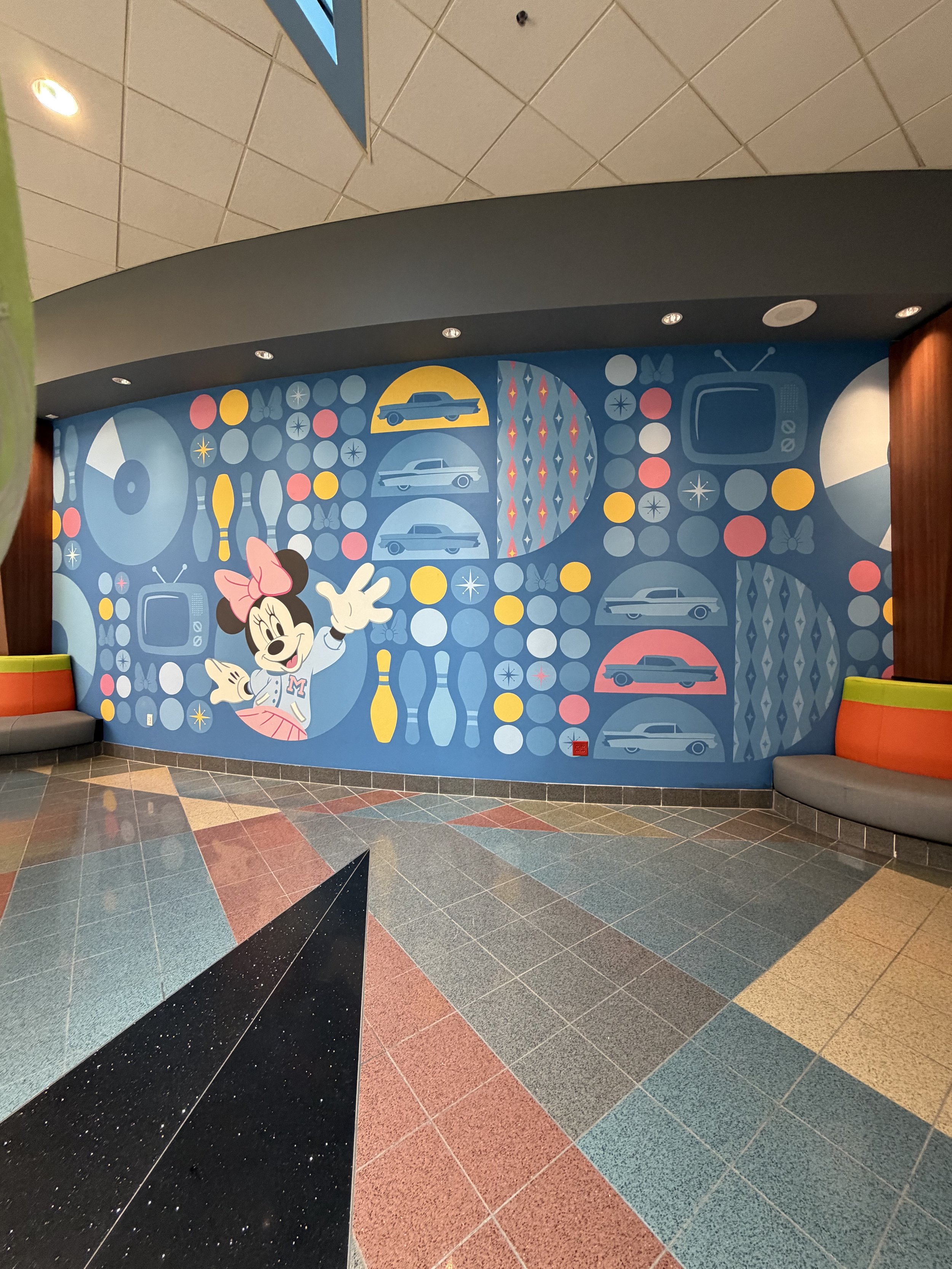 Colorful mural of Minnie Mouse waving, surrounded by retro car and television images, in a vibrant, decorative indoor space.