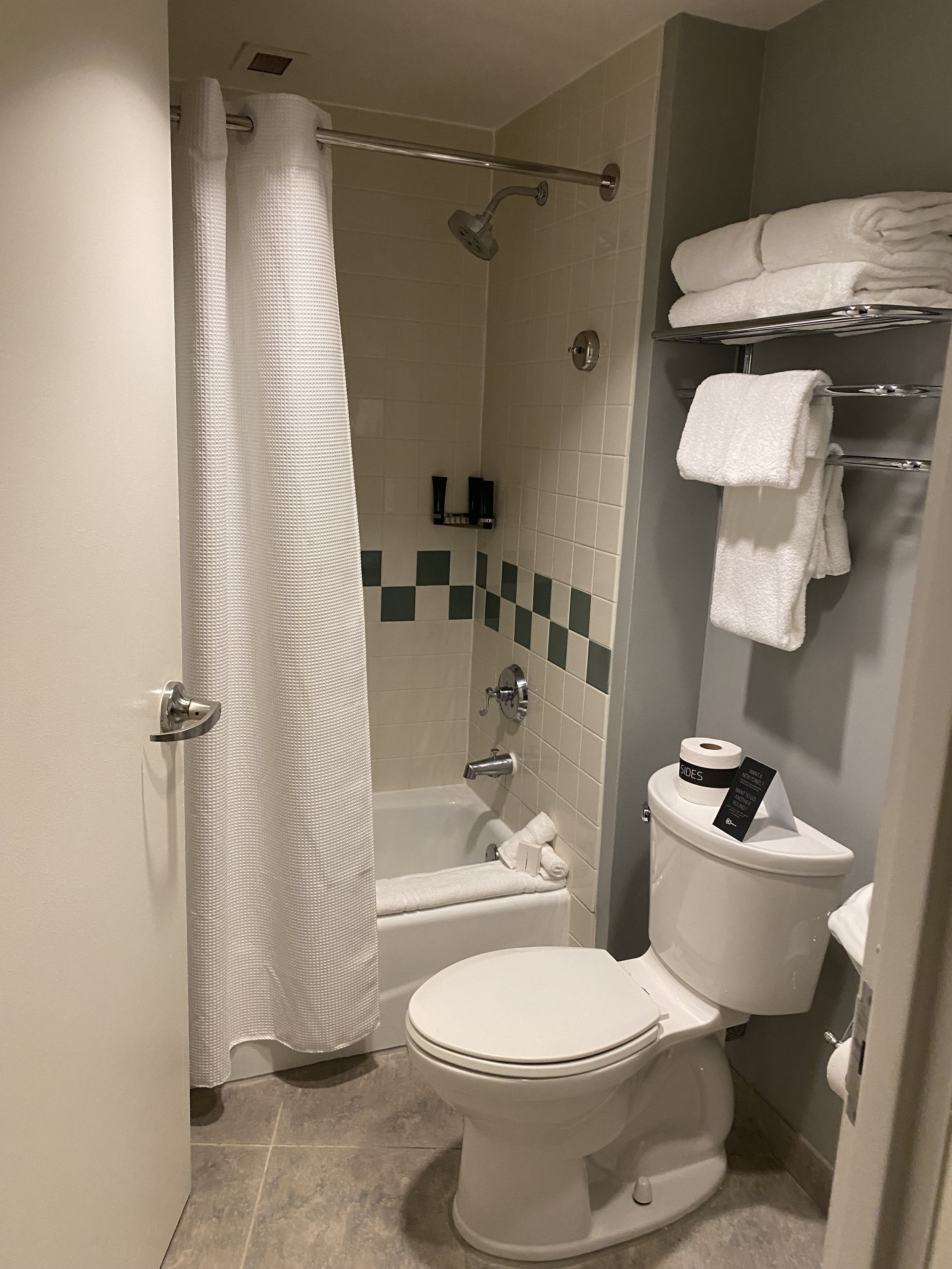 A small bathroom with a shower, a toilet, and shelves with towels.