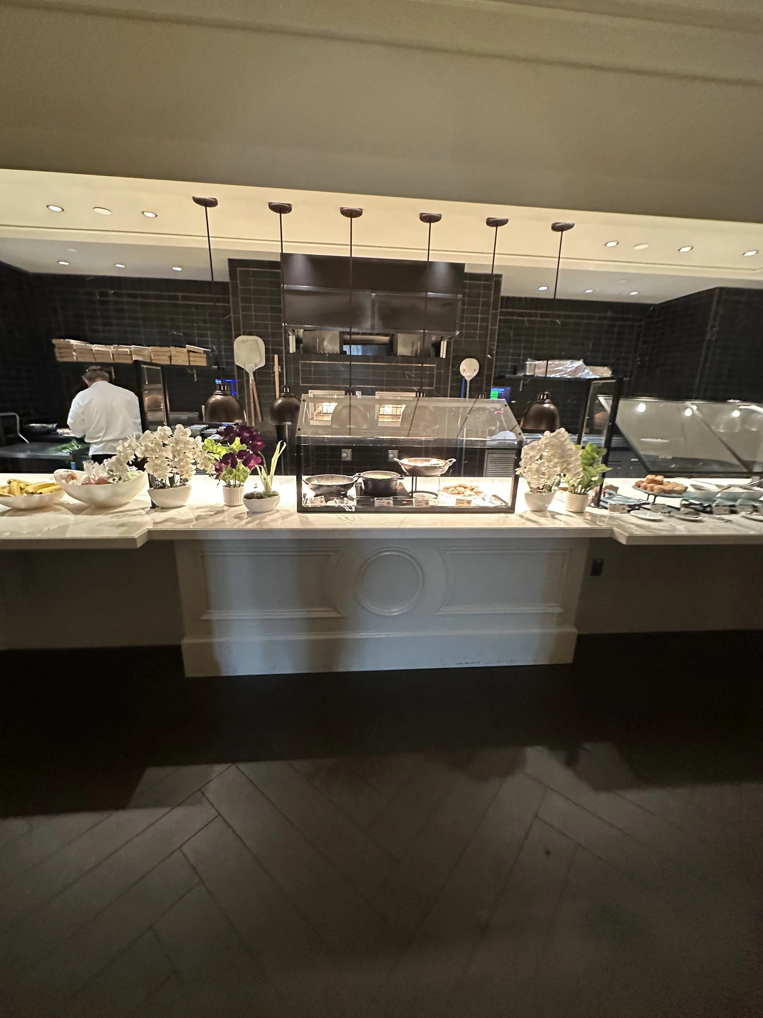 Buffet station with dishes, flowers, and a chef in the background at a restaurant.