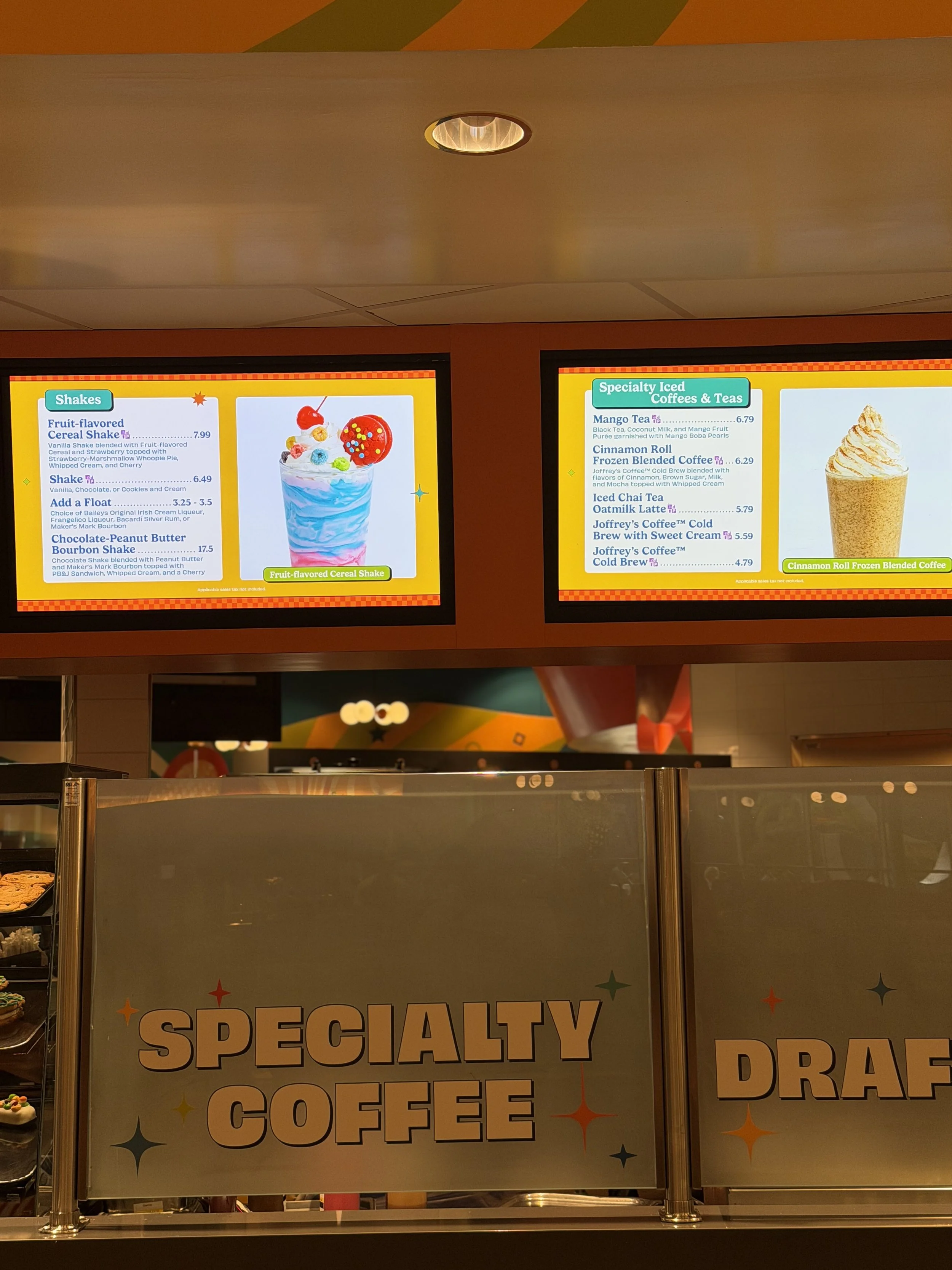 Five digital menu screens displaying drink options and prices at a specialty coffee shop. The counter has a sign with 'SPECIALTY COFFEE' visible.