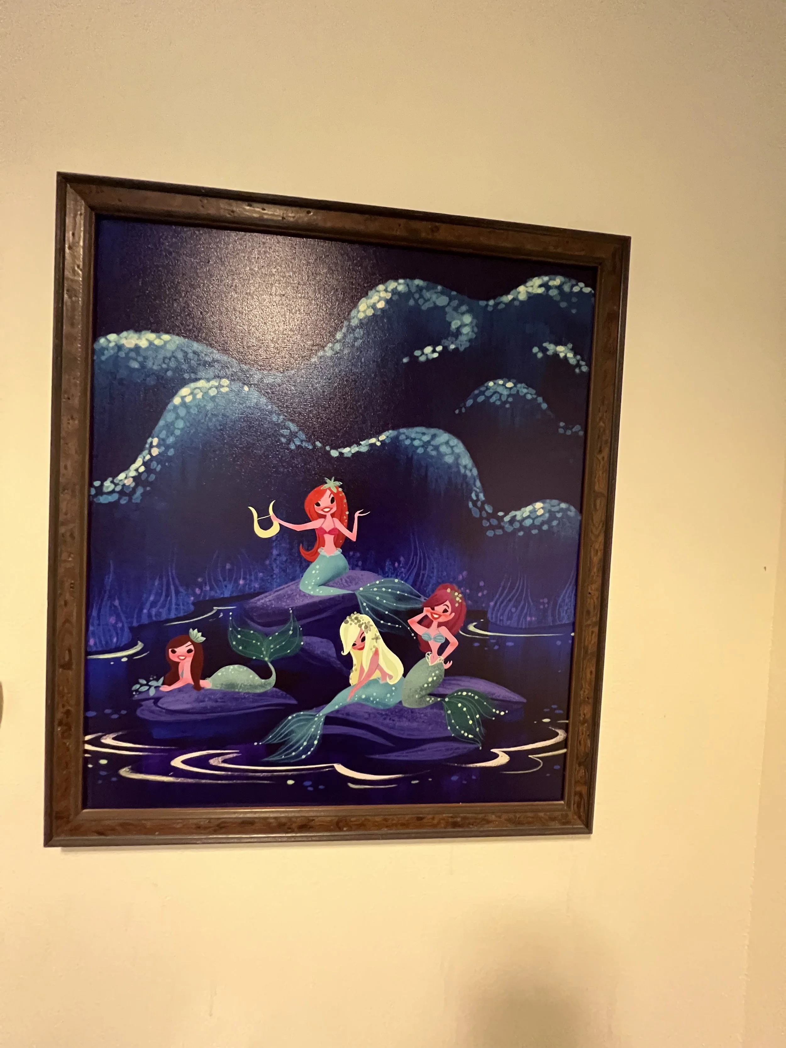Colorful illustration of four mermaids with various hair colors and styles, sitting on rocks in a dark blue, mystical water setting with starry, glowing waves in the background.