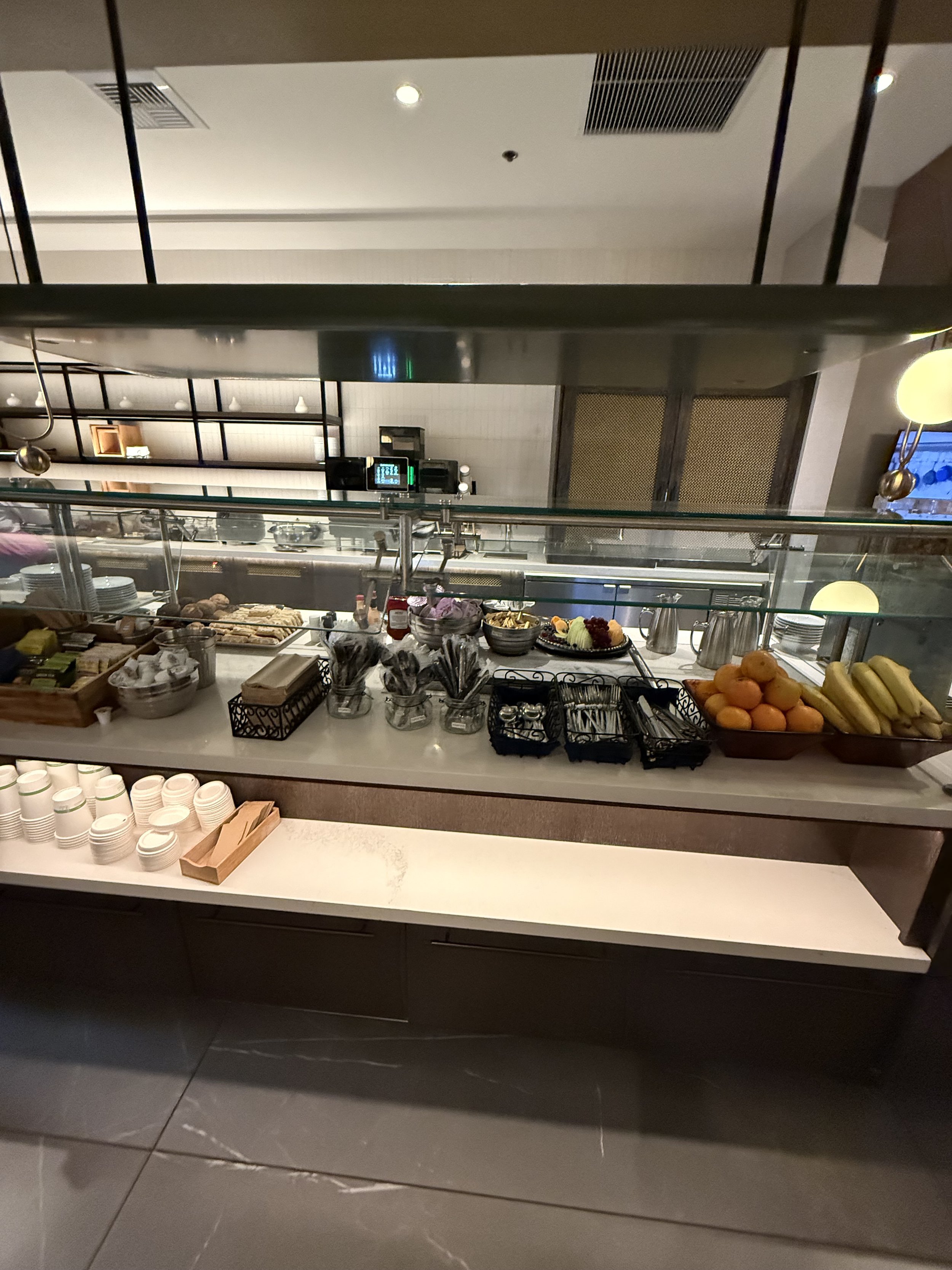 Hotel breakfast buffet with bowls of fruit, pastries, and condiments behind a glass counter.