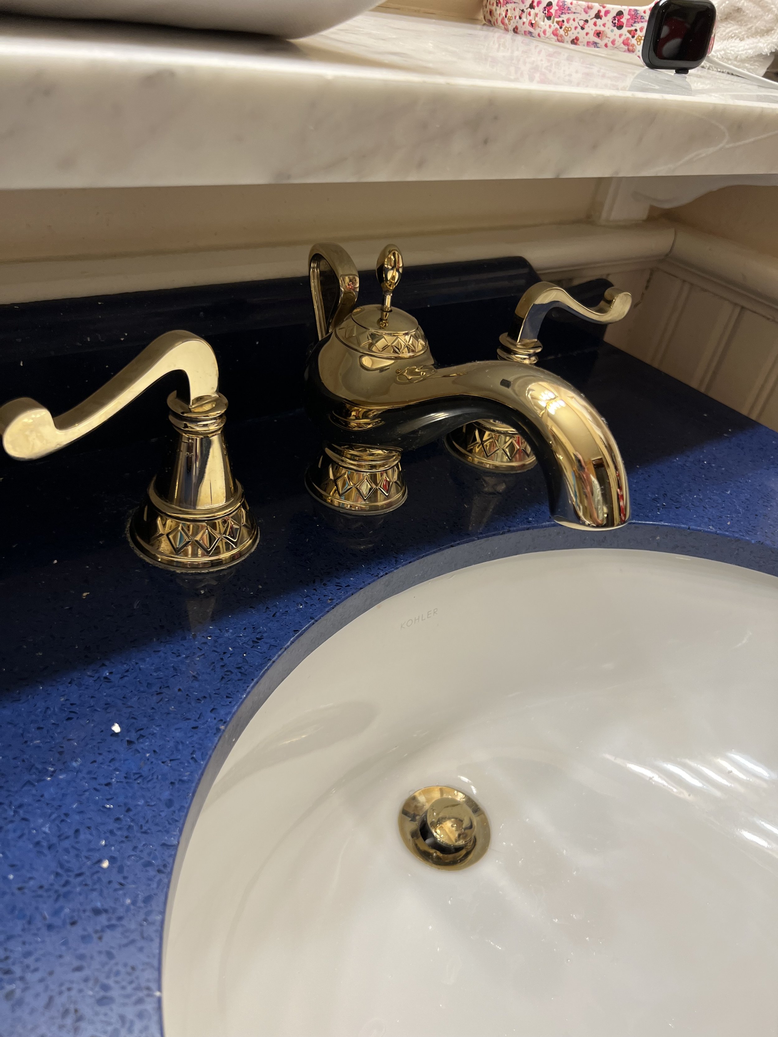Close-up of a gold-colored faucet and handles on a blue bathroom sink with a white basin and marble countertop.