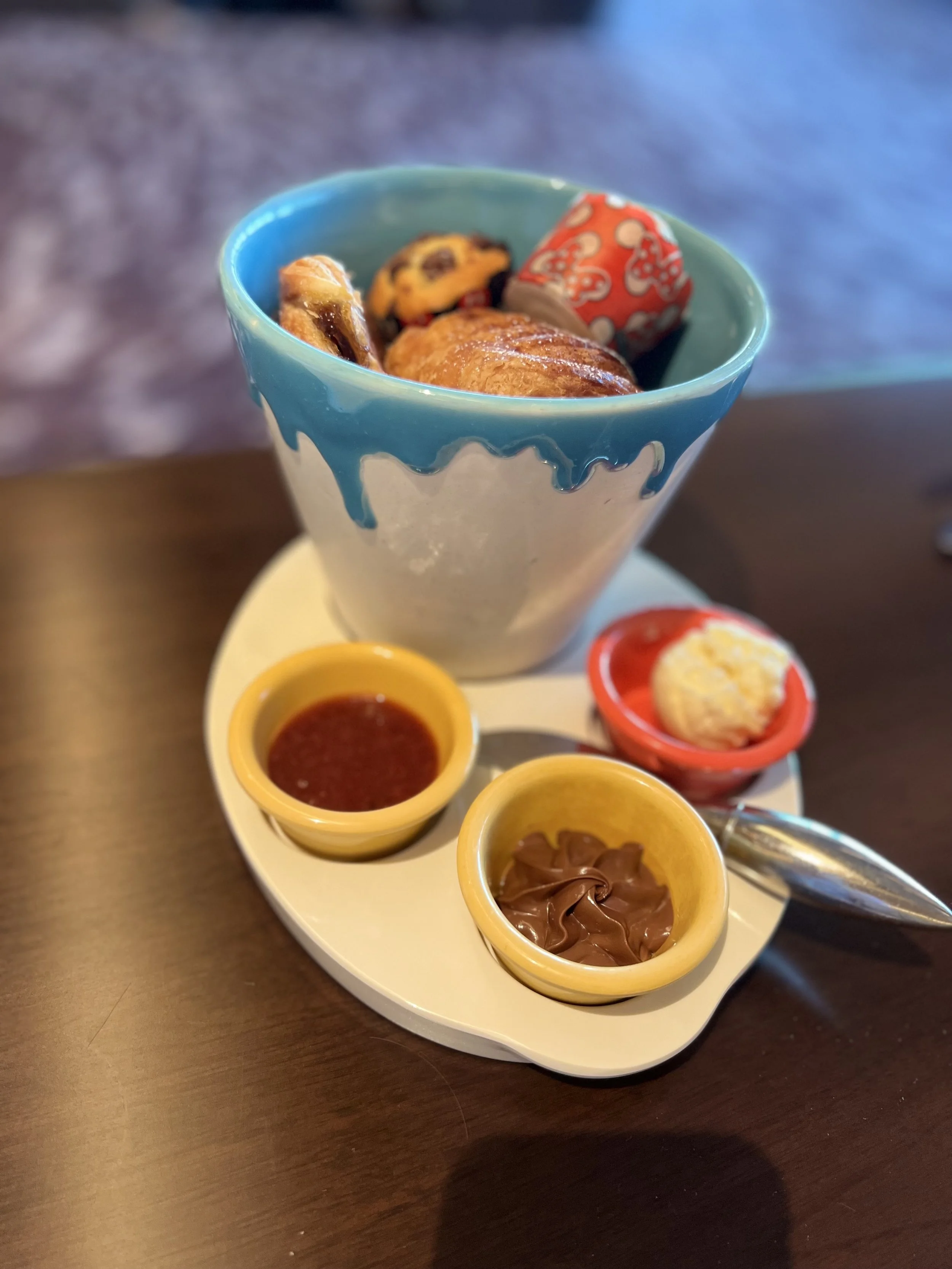 A bowl of assorted chocolates and pastries with small bowls of sauce and spread, served on a white plate with a silver spoon.