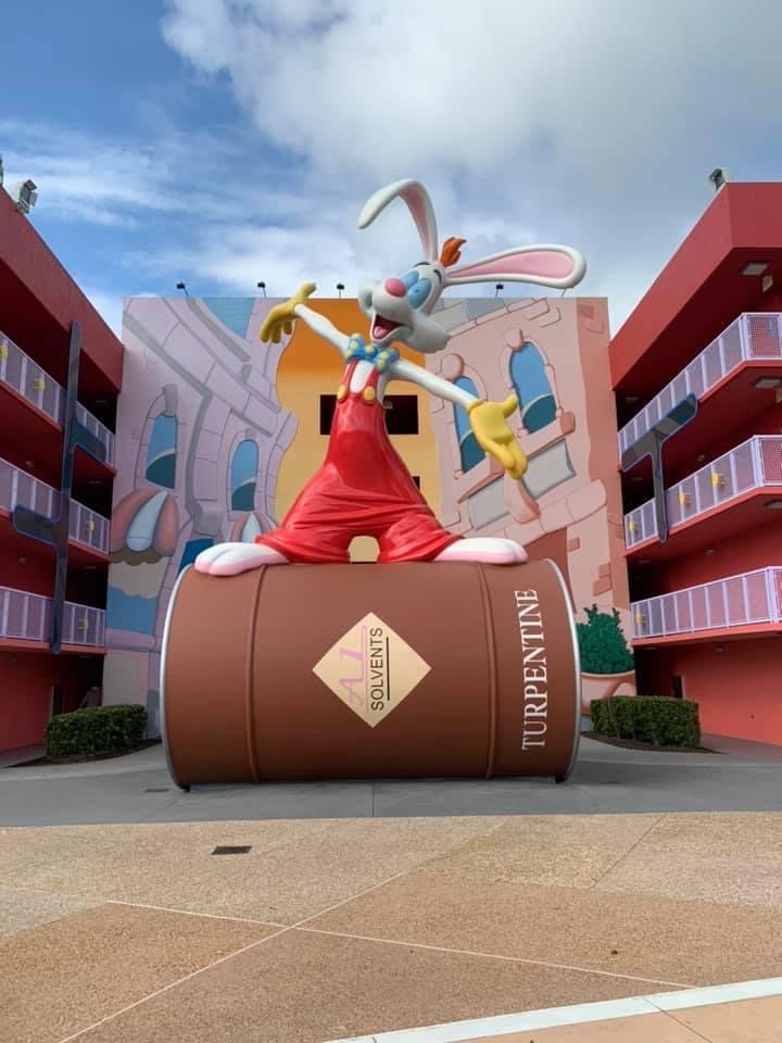 Large cartoon statue of Bugs Bunny holding a paintbrush, standing on a giant medicine bottle labeled 'Solvents' and 'Turpentine', in front of colorful buildings and a partly cloudy sky.