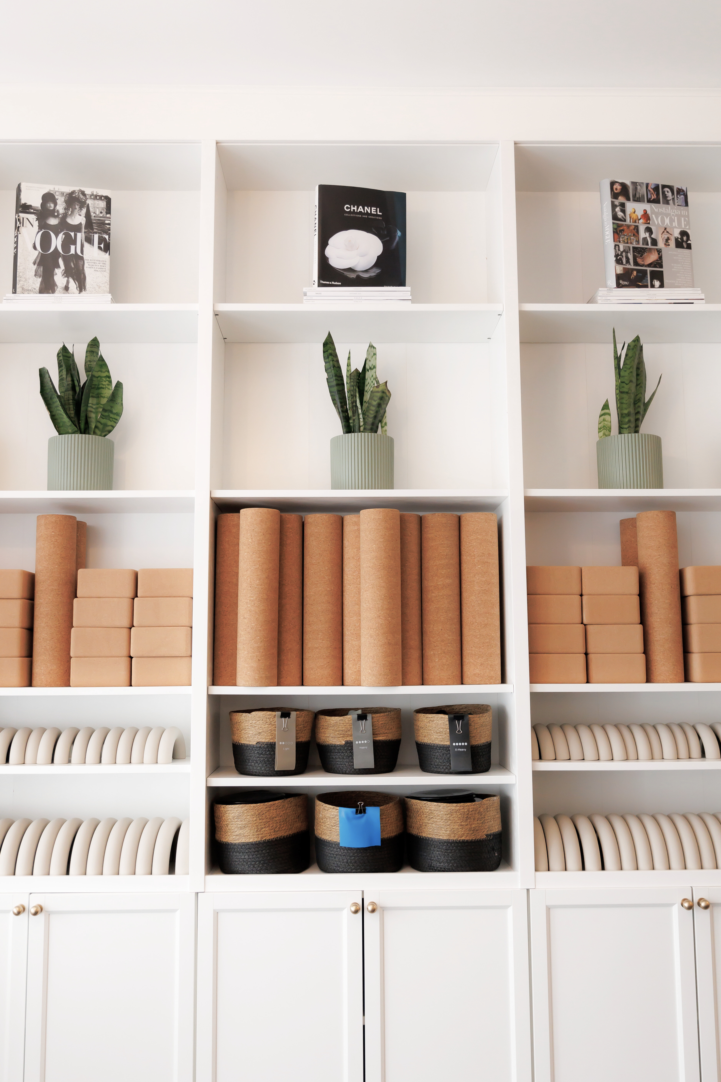 White bookshelf with plants, books, and storage baskets. Pilates and barre studio in The Junction, Toronto.