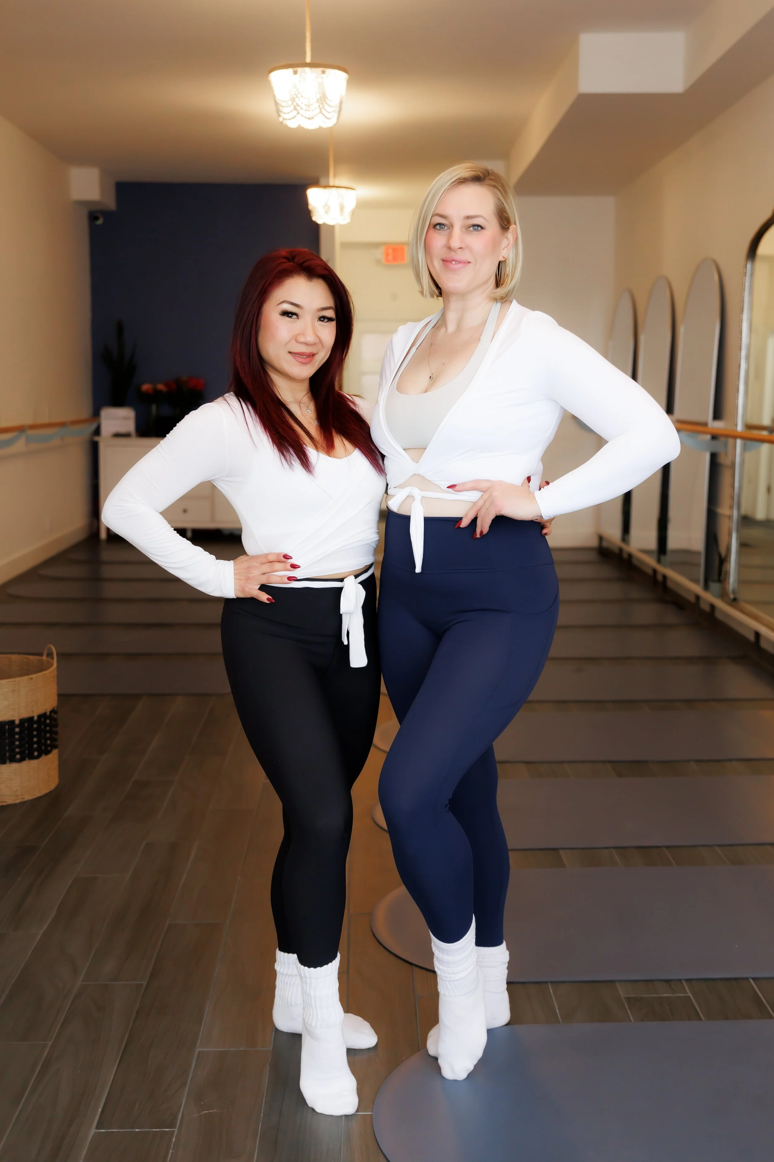 Two women in athletic wear standing in a fitness studio, smiling at the camera. Pilates and barre studio in The Junction, Toronto. Pilates and barre studio in The Junction, Toronto.