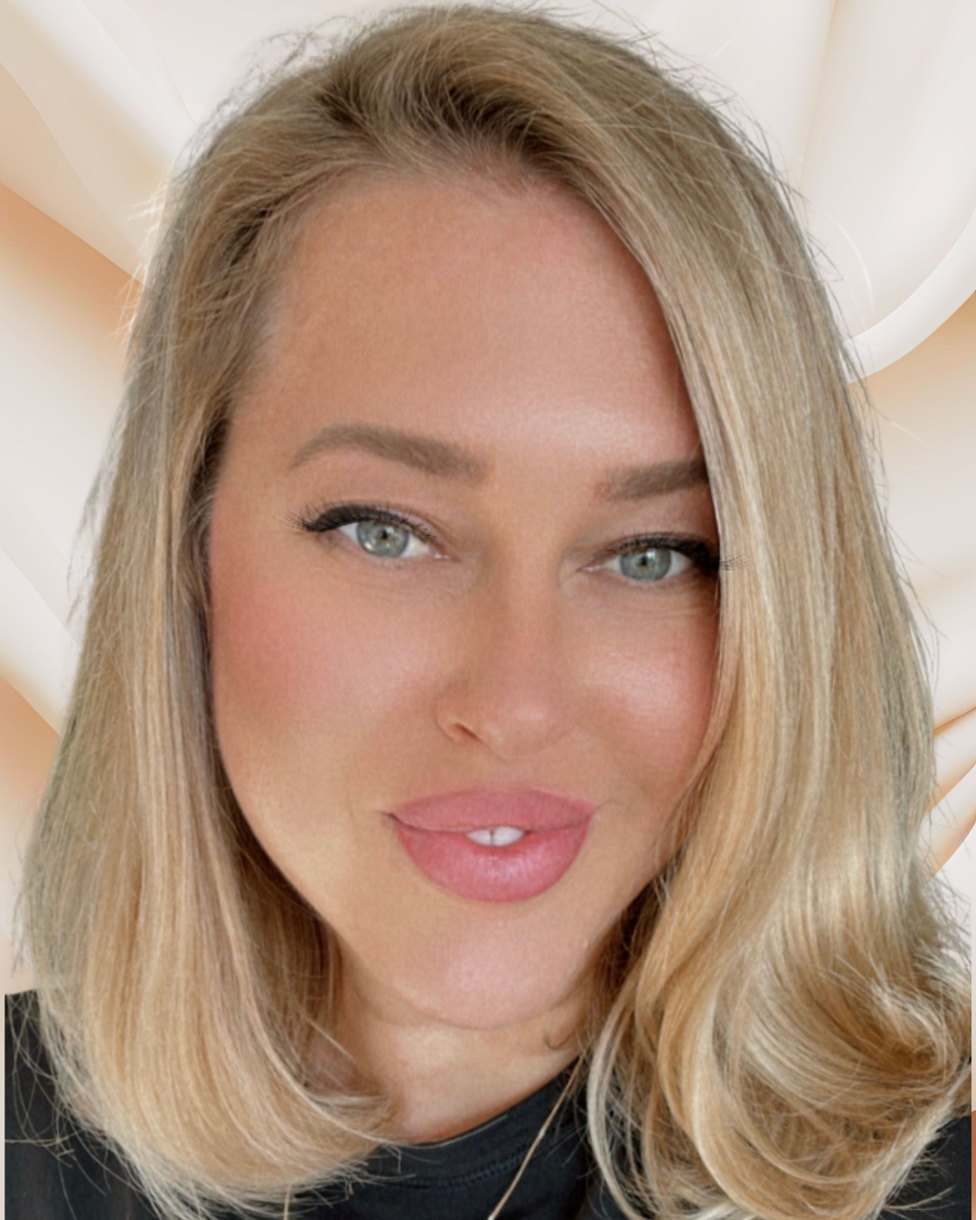 Close-up photo of a woman with blonde hair, blue eyes, and makeup, smiling slightly with a soft background. Pilates and barre studio in The Junction, Toronto.