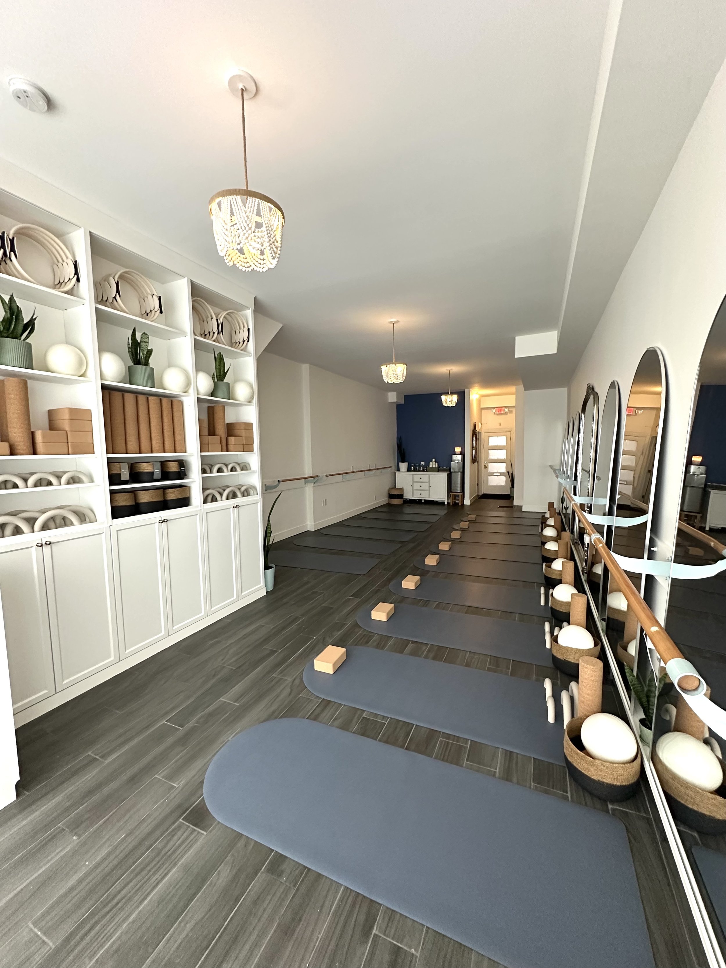 Yoga studio with mats, blocks, and props arranged on the floor, mirrors on the wall, and shelves with decorative items and yoga accessories. Pilates and barre studio in The Junction, Toronto.