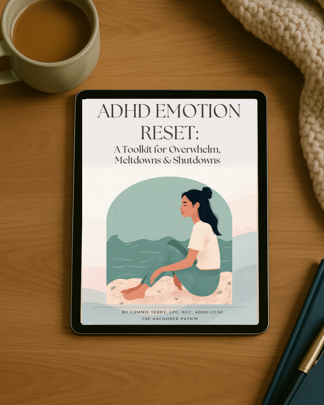 Digital tablet displaying a book cover titled 'ADHD Emotion Reset: A Toolkit for Overwhelm, Meltdowns & Shutdowns' with an illustration of a woman sitting with her eyes closed near waves on a beach. The tablet is on a wooden desk with a cup of coffee, a notebook, and a pen nearby, and a cozy blanket in the top right corner.