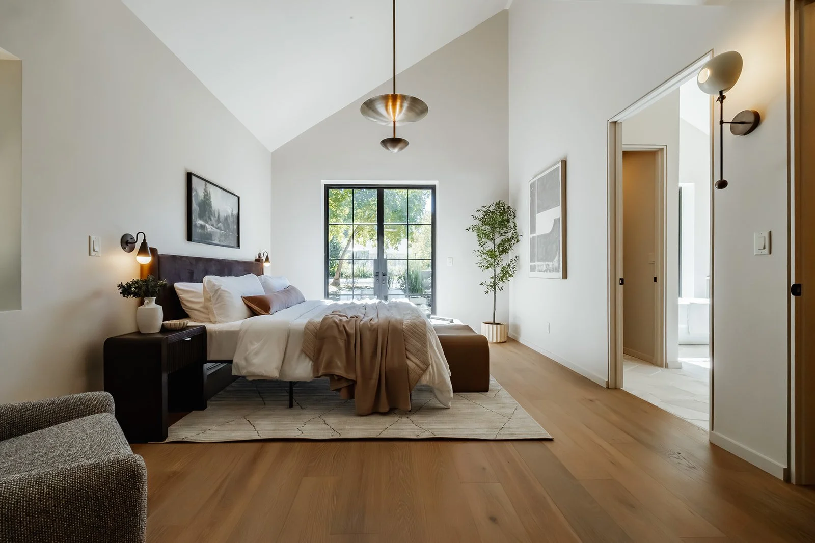 Modern bedroom with a large bed, neutral bedding, a black nightstand, framed artwork, a window, and hardwood floors.