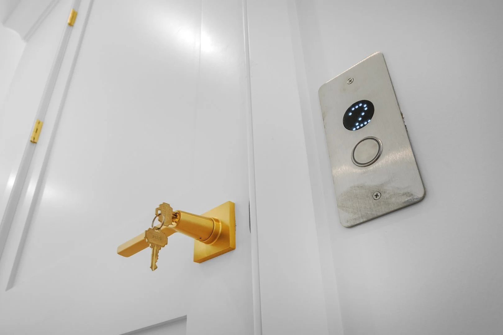 Indoor elevator control panel with illuminated circular display and call button next to a yellow handle with a key attached, mounted on a white wall.