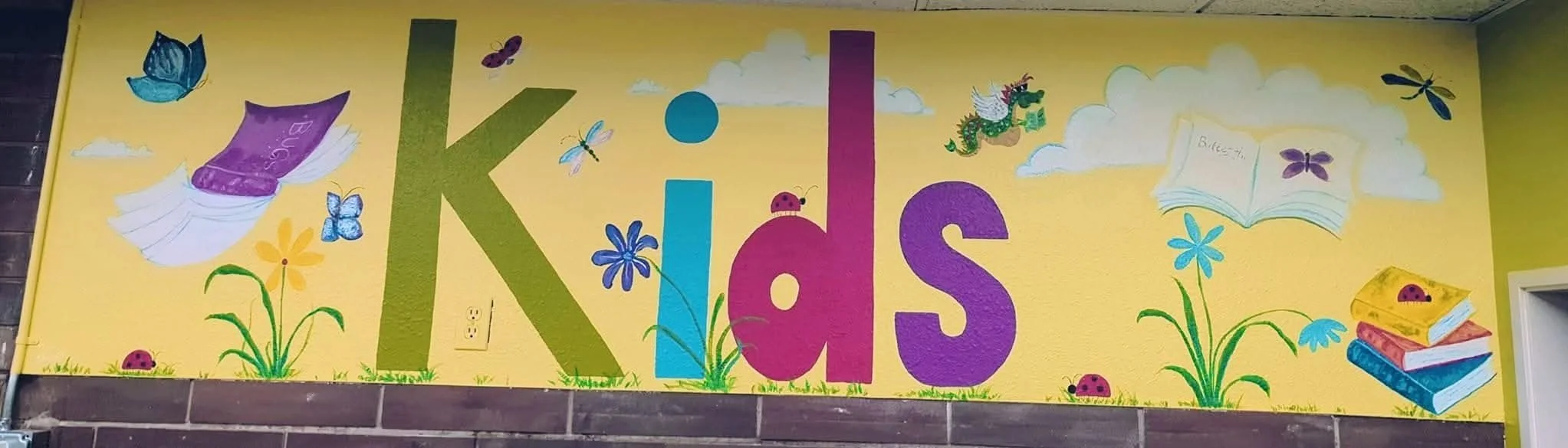 Mural painted with word kids and butterflies, dragonflies and flying books.