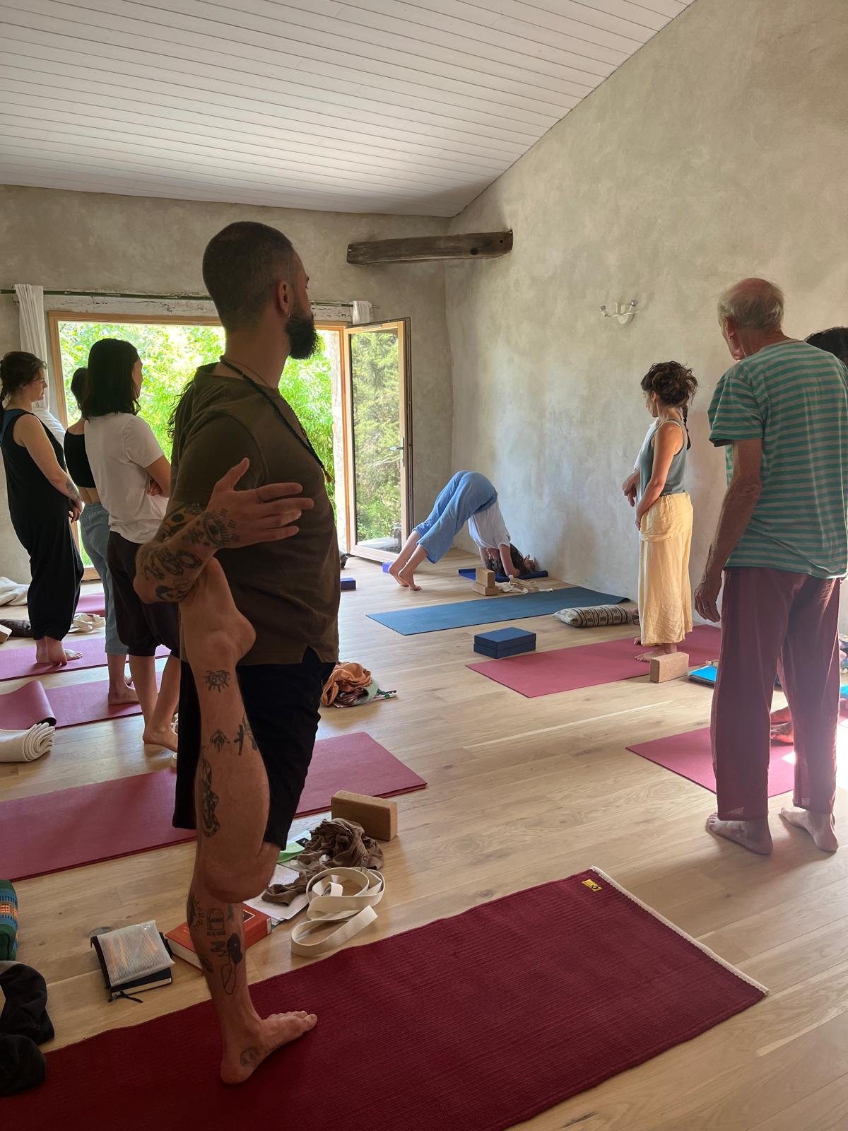 Groupe de personnes participant à un cours de yoga dans une pièce lumineuse avec ouverture sur un jardin verdoyant au Domaine de Maynard.