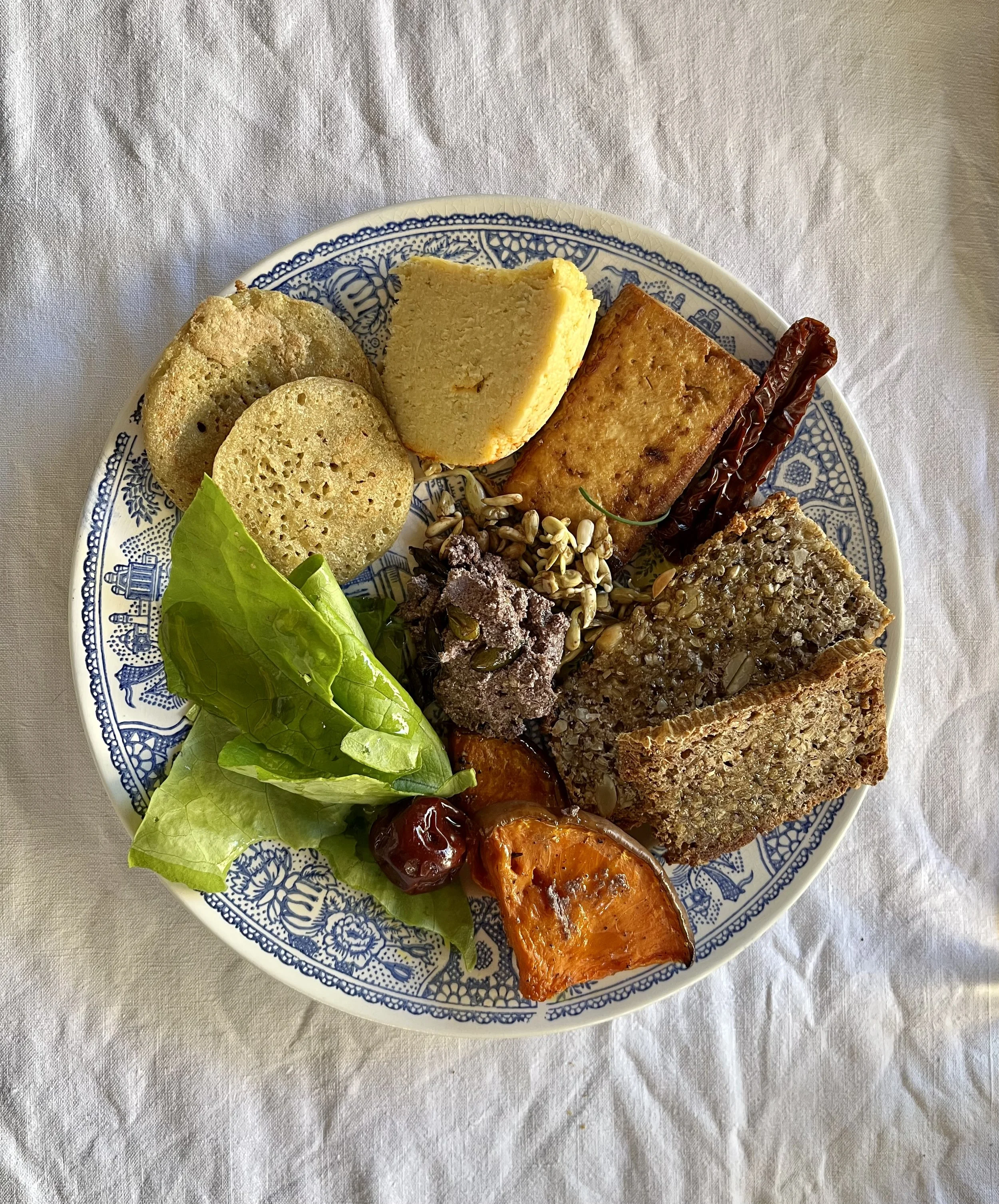 Assiette de divers aliments végétariens ou végétaliens, inclus des morceaux de pain, de tofu, de légumes grillés, des graines, de la salade et des dattes. Cuisine ayurvédique au Domaine de Maynard, gite de groupe.