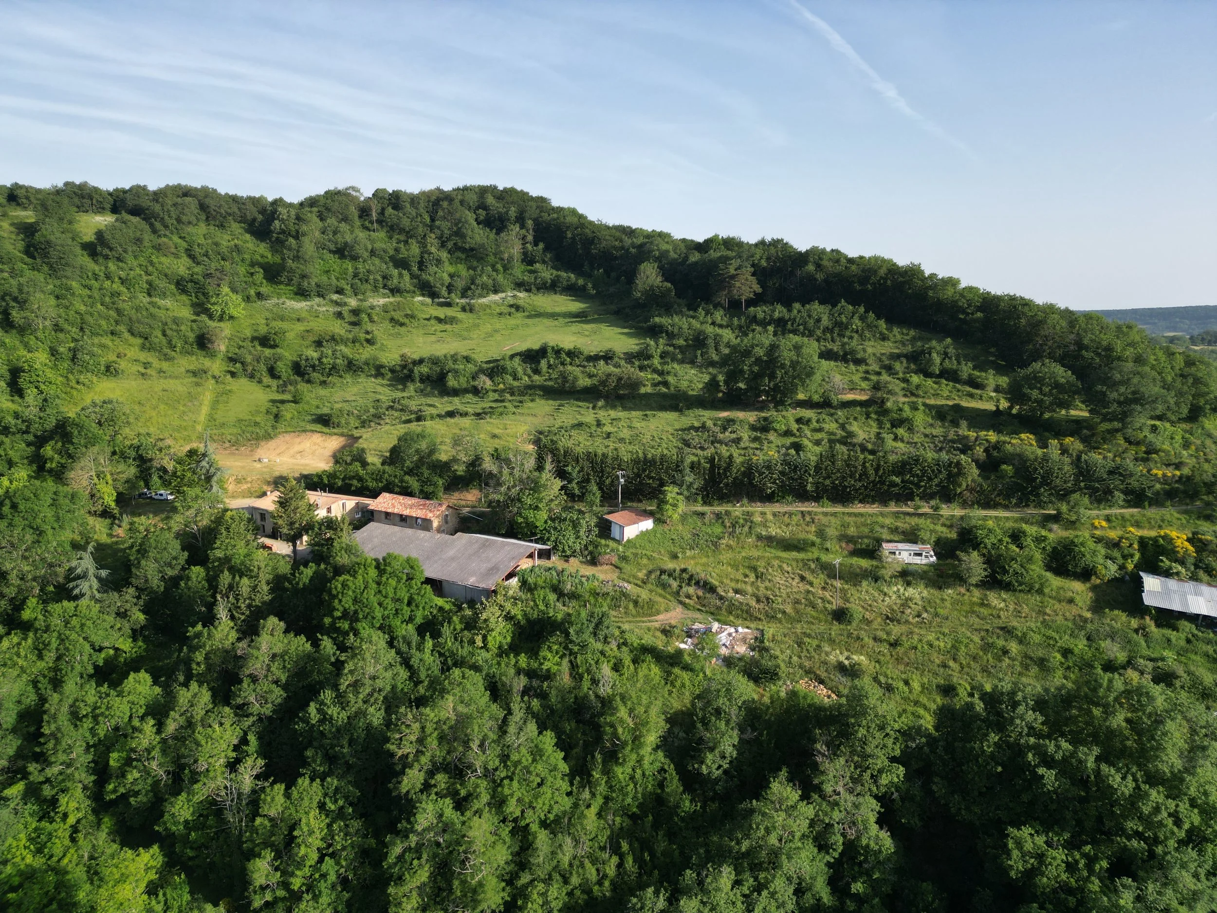 Vue aérienne d'une ferme entourée de verdure et de collines boisées sous un ciel clair. Le Domaine de Maynard est parfait pour des stages et retraitres de groupe.