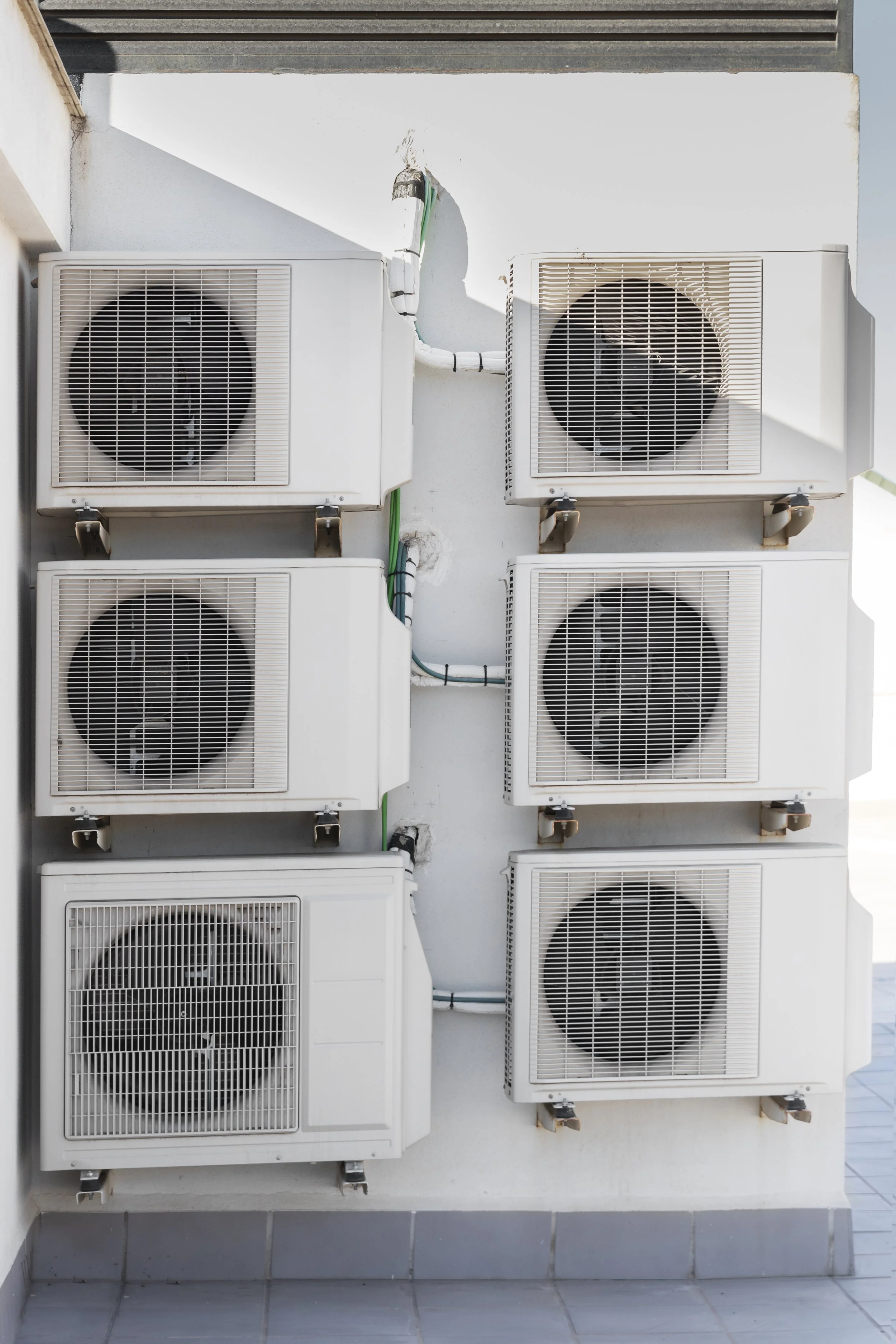 Six air conditioning units mounted on an exterior white wall.