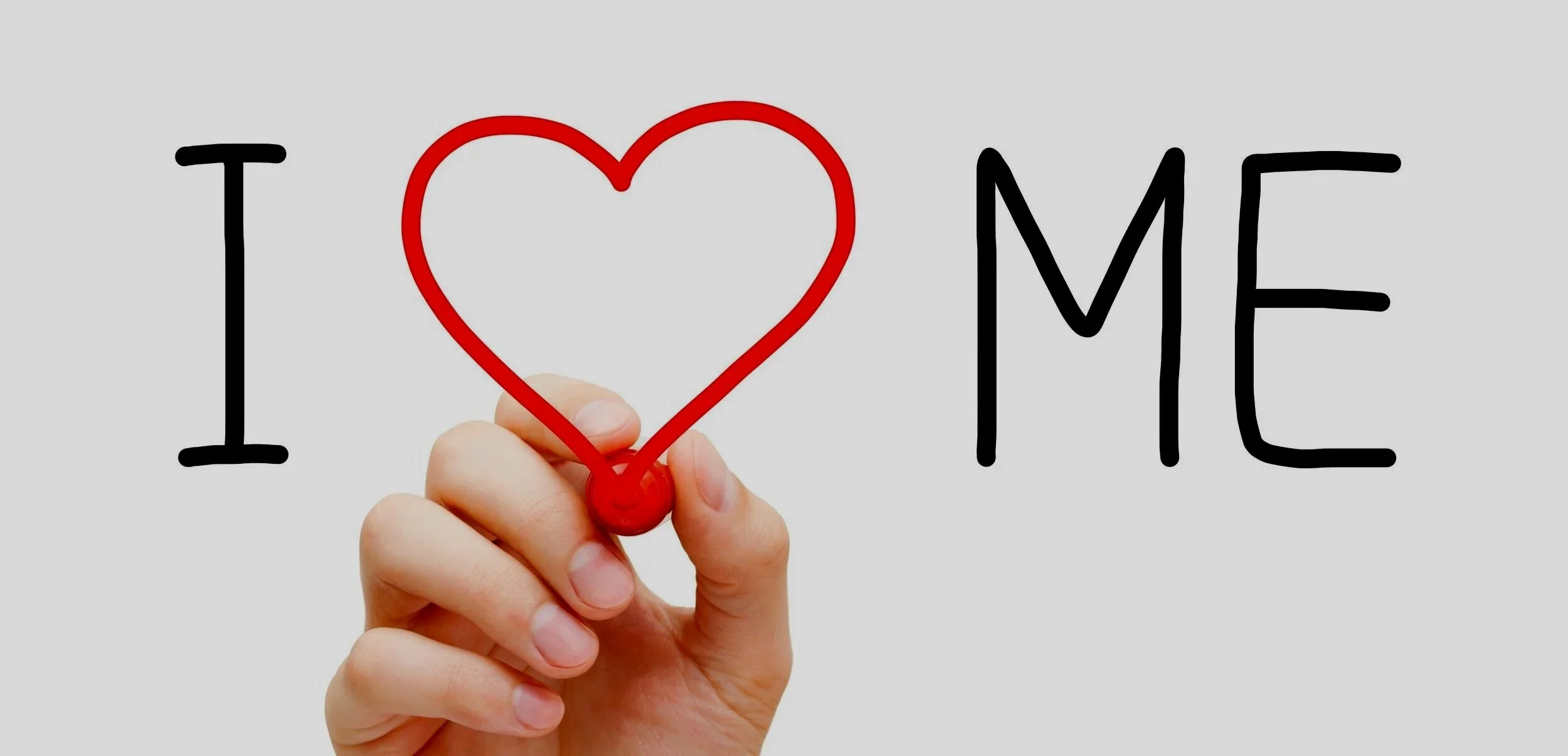 A hand holding a red heart-shaped marker under the words "I" and "ME" to create the phrase "I love me"