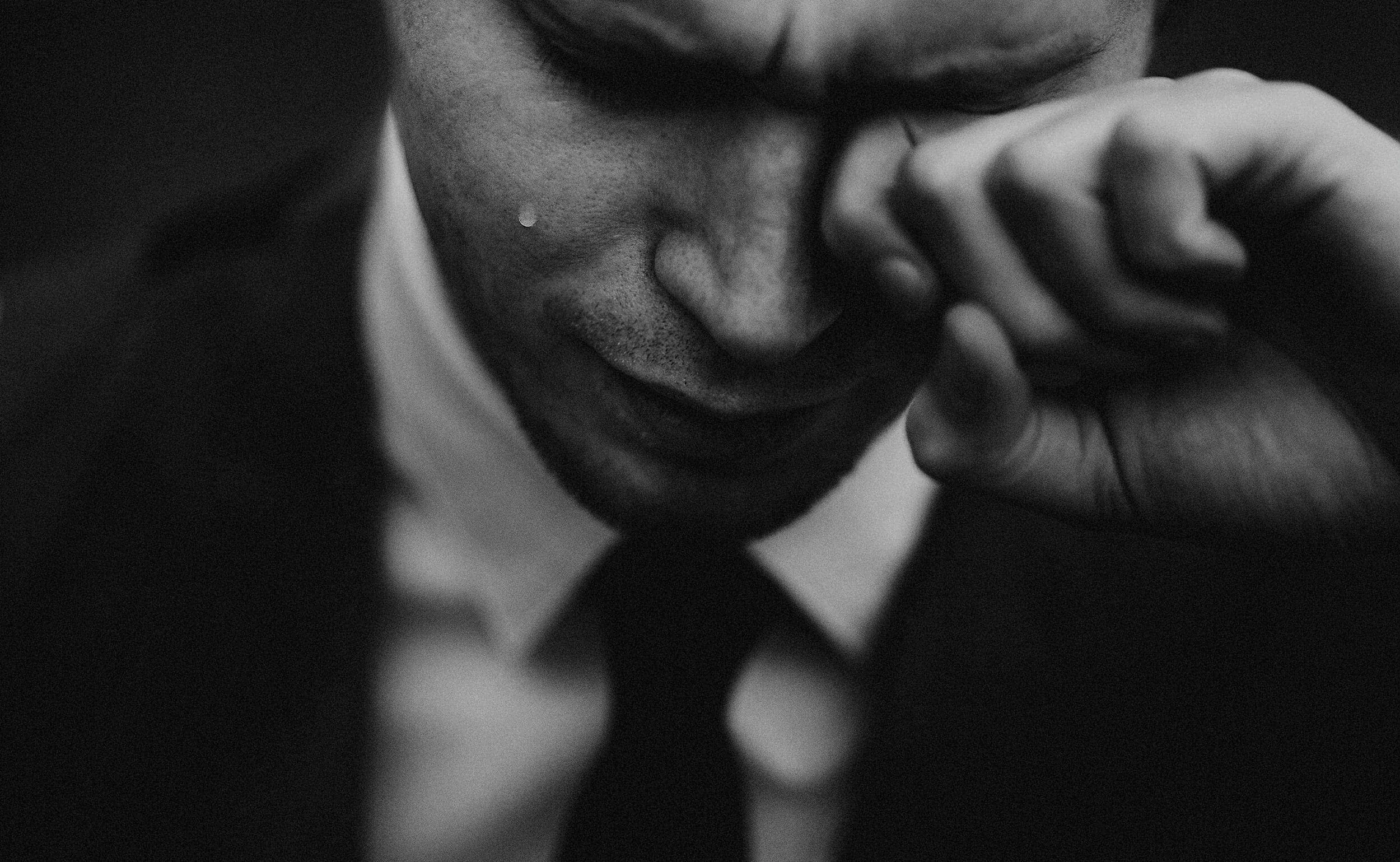 Close-up of an emotional man in a suit touching his face, with a tear running down his cheek, in black and white.