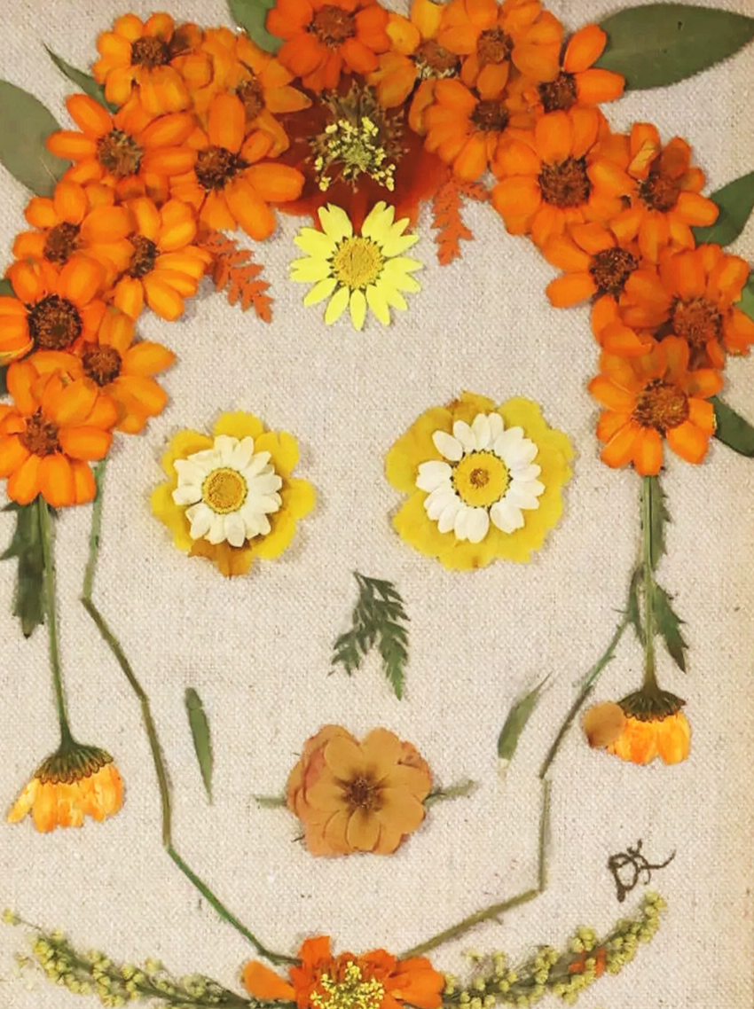 Arrangement of various orange, yellow, and white flowers and green leaves, forming a face-like pattern.