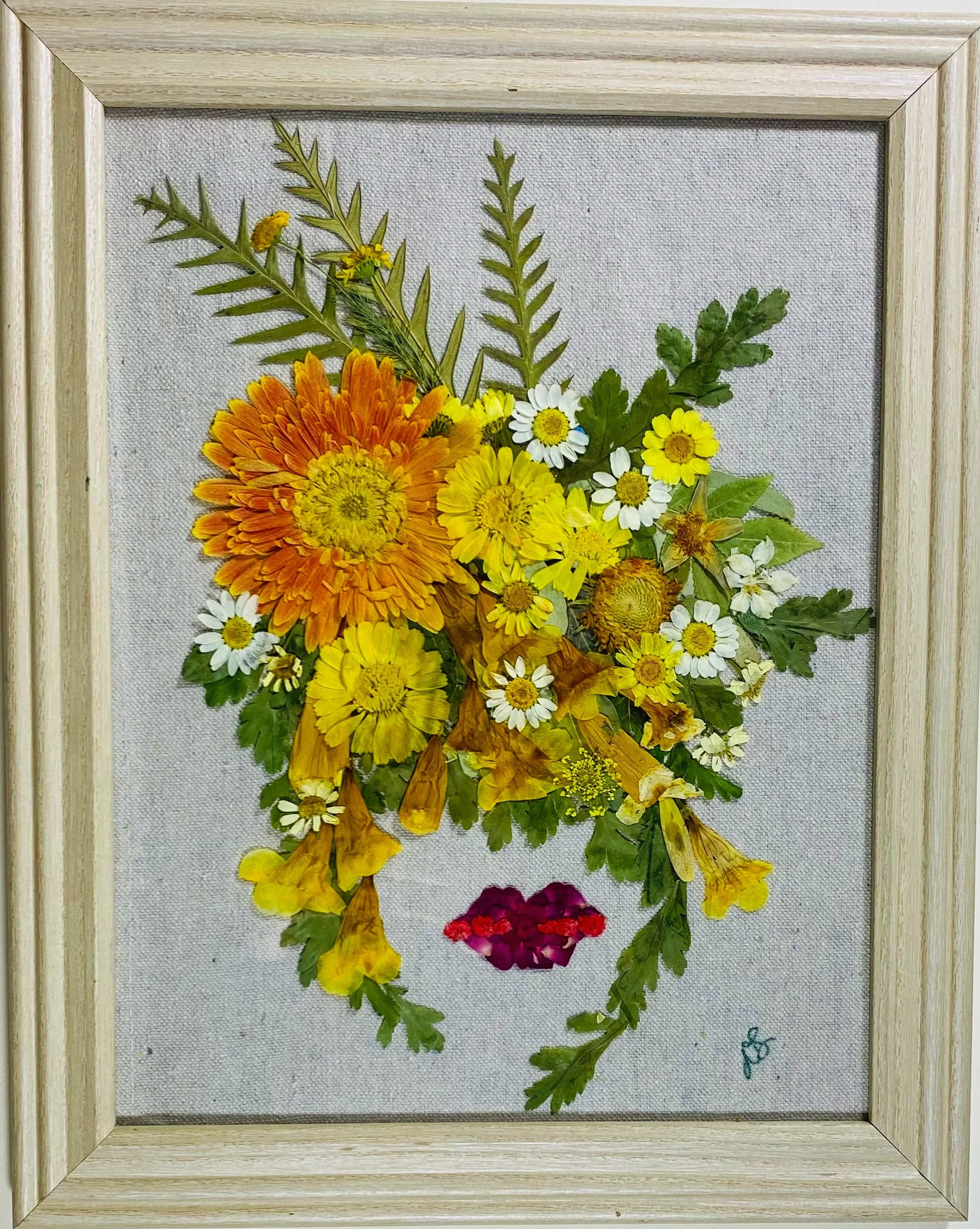 Artwork made with pressed flowers in a wooden frame, depicting a feminine face with floral hair and lips.
