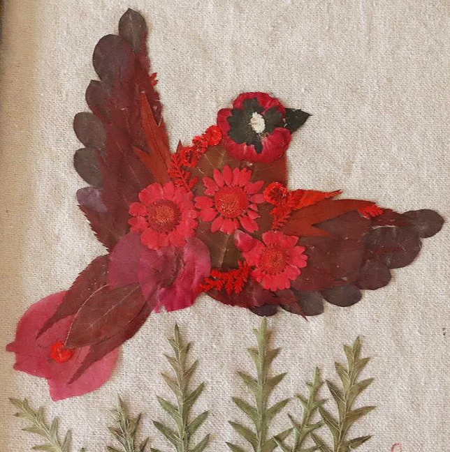 A bird crafted from red flowers and leaves mounted on a canvas background.