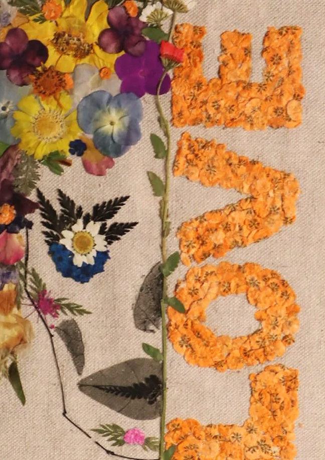Arrangement of colorful flowers and orange floral letters spelling 'LOVE' on fabric background.