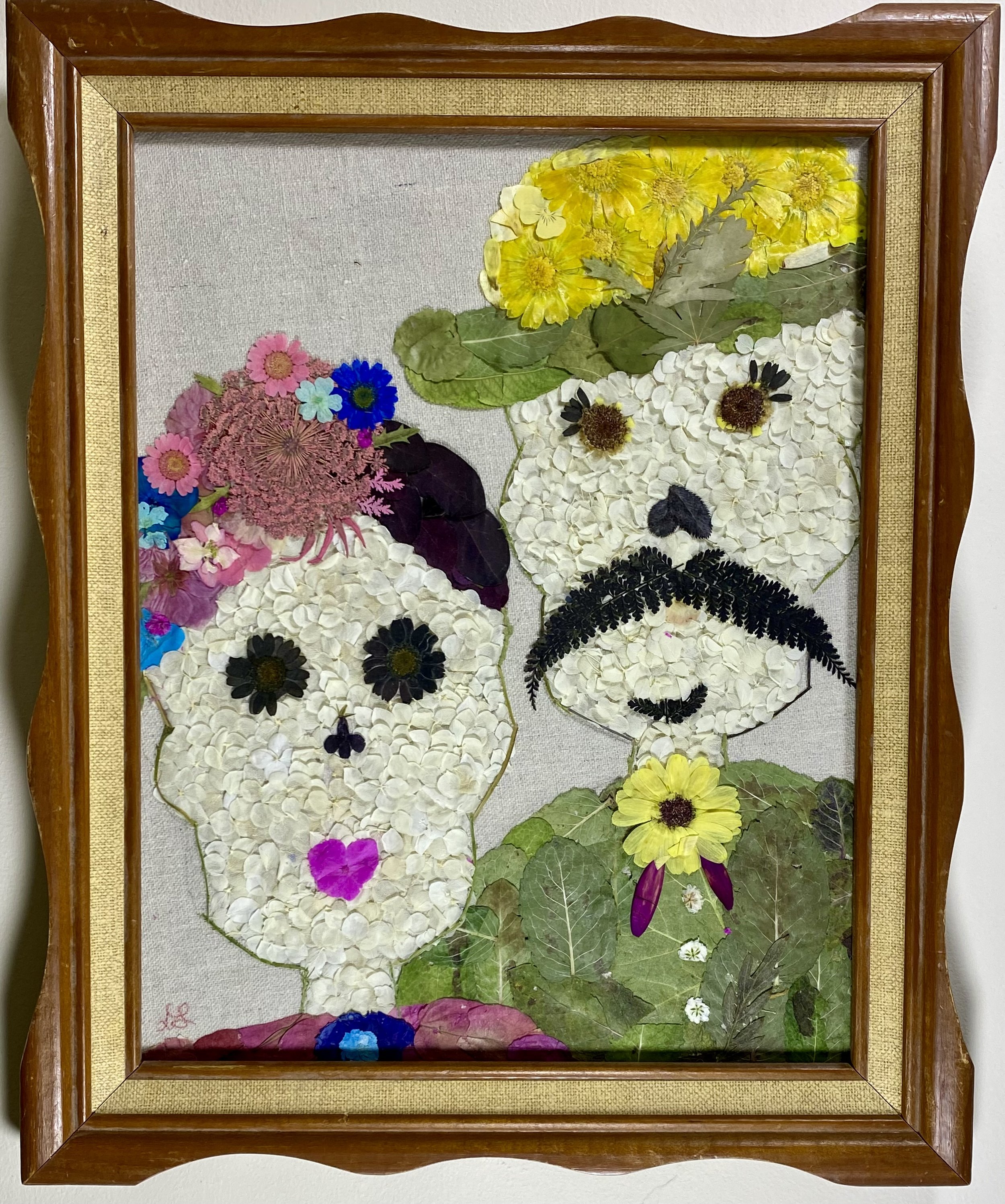 A framed artwork made of pressed flowers depicting two dog faces with floral details and leaves.