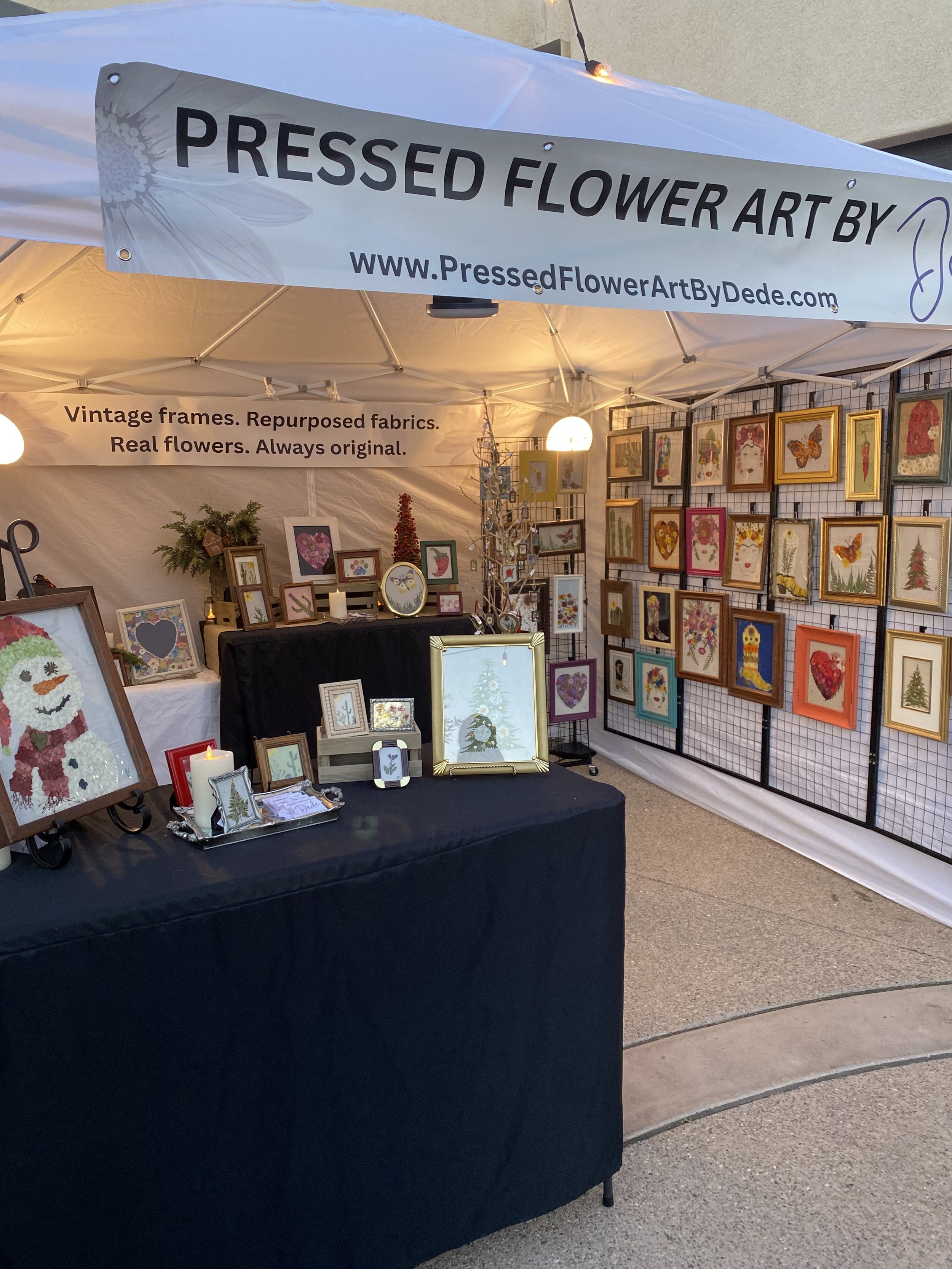 A booth displaying pressed flower art at an outdoor craft fair or market.