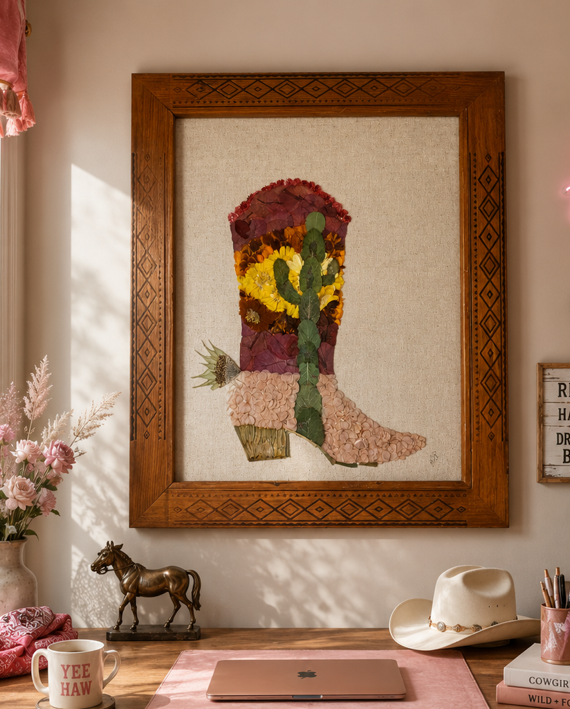 A framed quilted artwork of a cactus in a pot, with sunflower accents, hanging on a wall in a decorated room.