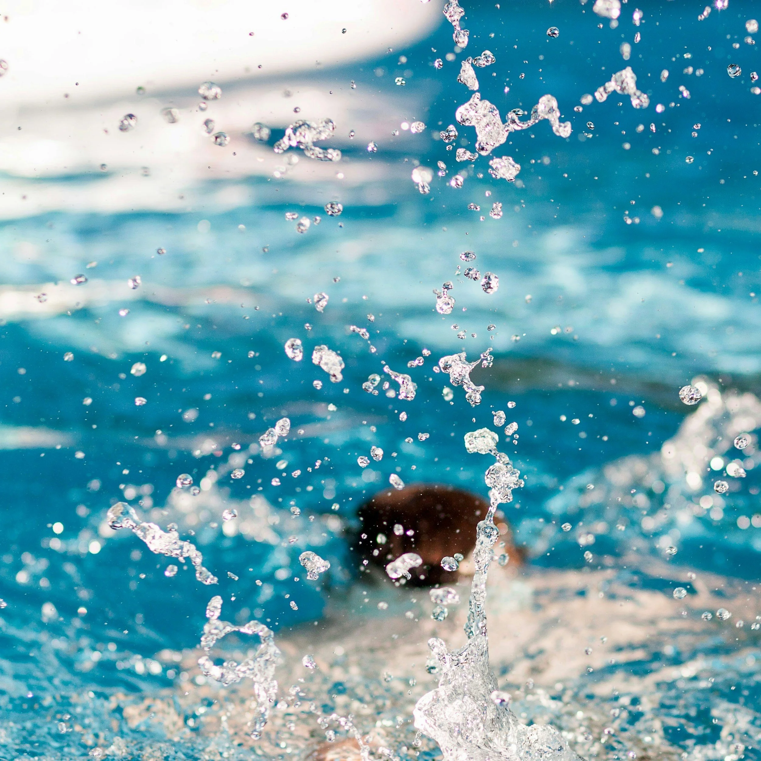 A person swimming in a pool with water splashing around as they emerge from underwater.